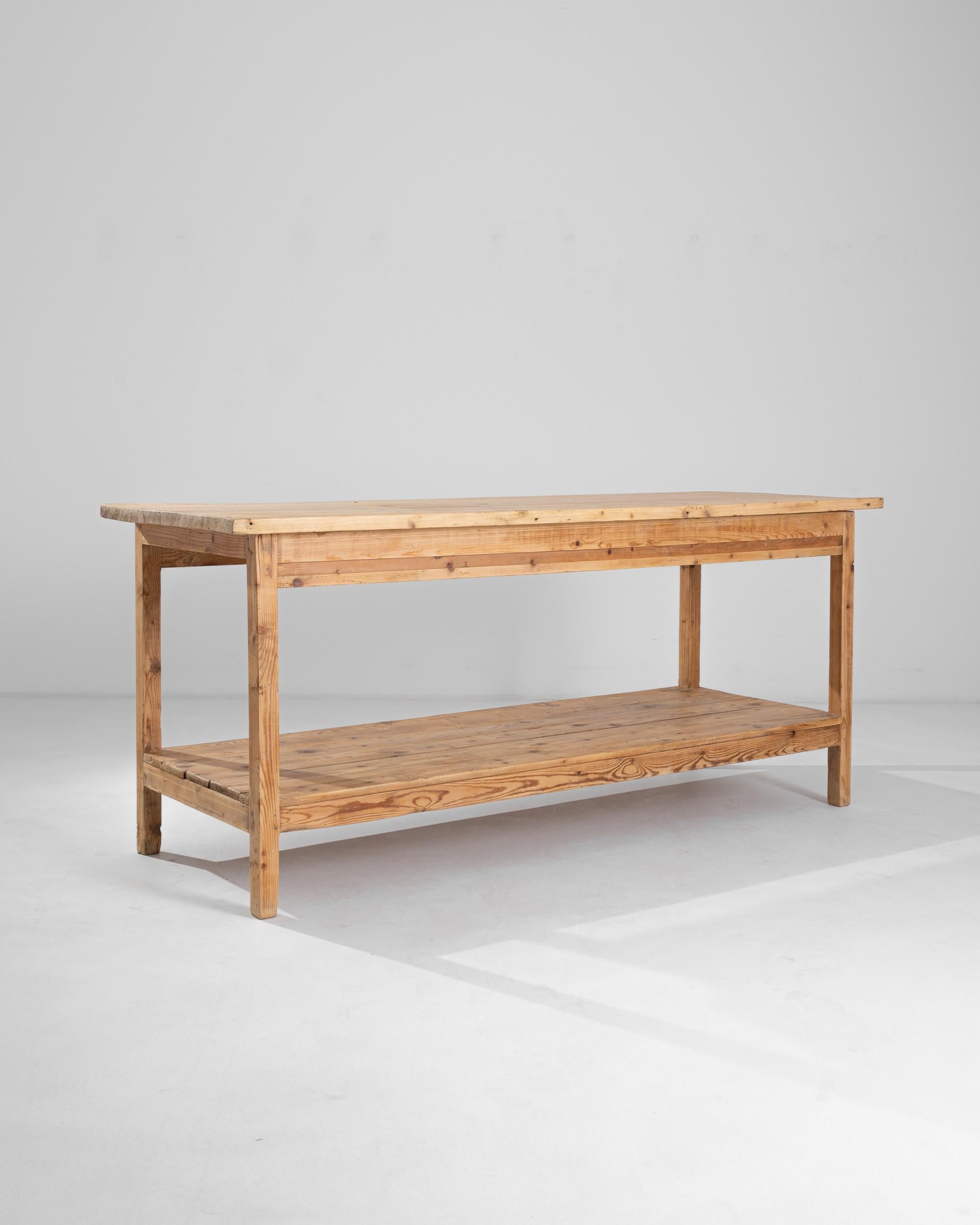 A Central European wooden table from the 20th century. This table is composed of long, bright planks of wood that form an expansive top and lower shelf. Subtle but complex wood grain shines quietly across its structure, emitting a hardworking and