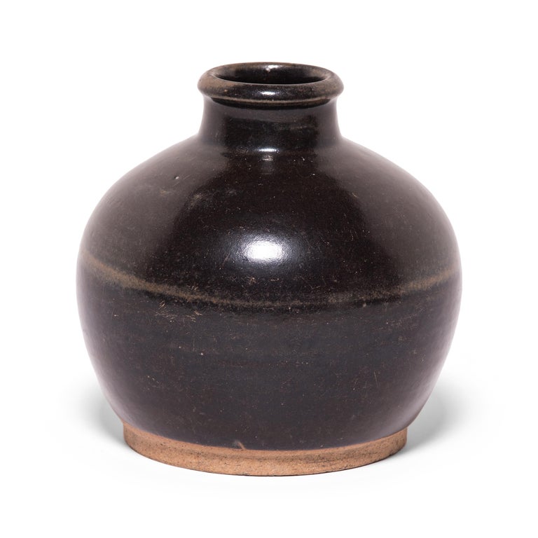 A rich brown glaze coats surface of this round wine jar, interrupted only by a sweep of light brown around the widest point. Crafted in the early 20th century, the jar was once used in a Qing dynasty apothecary to store wines infused with medicinal