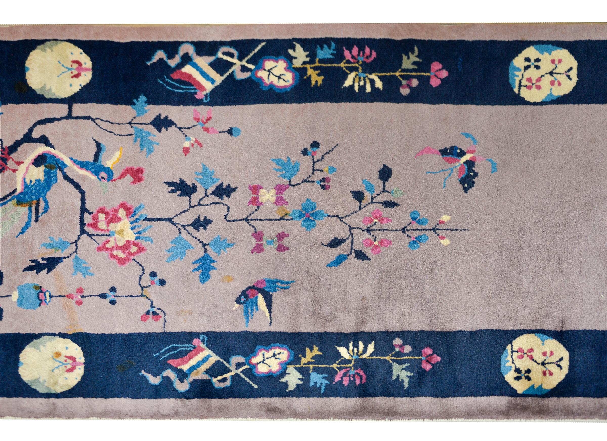 An early 20th century Chinese Art Deco runner with a central medallion depicting a vase potted with a flowering lotus, and flowering trees on either end, and all set abasing a gray field with a wide indigo striped border with a floral pattern.