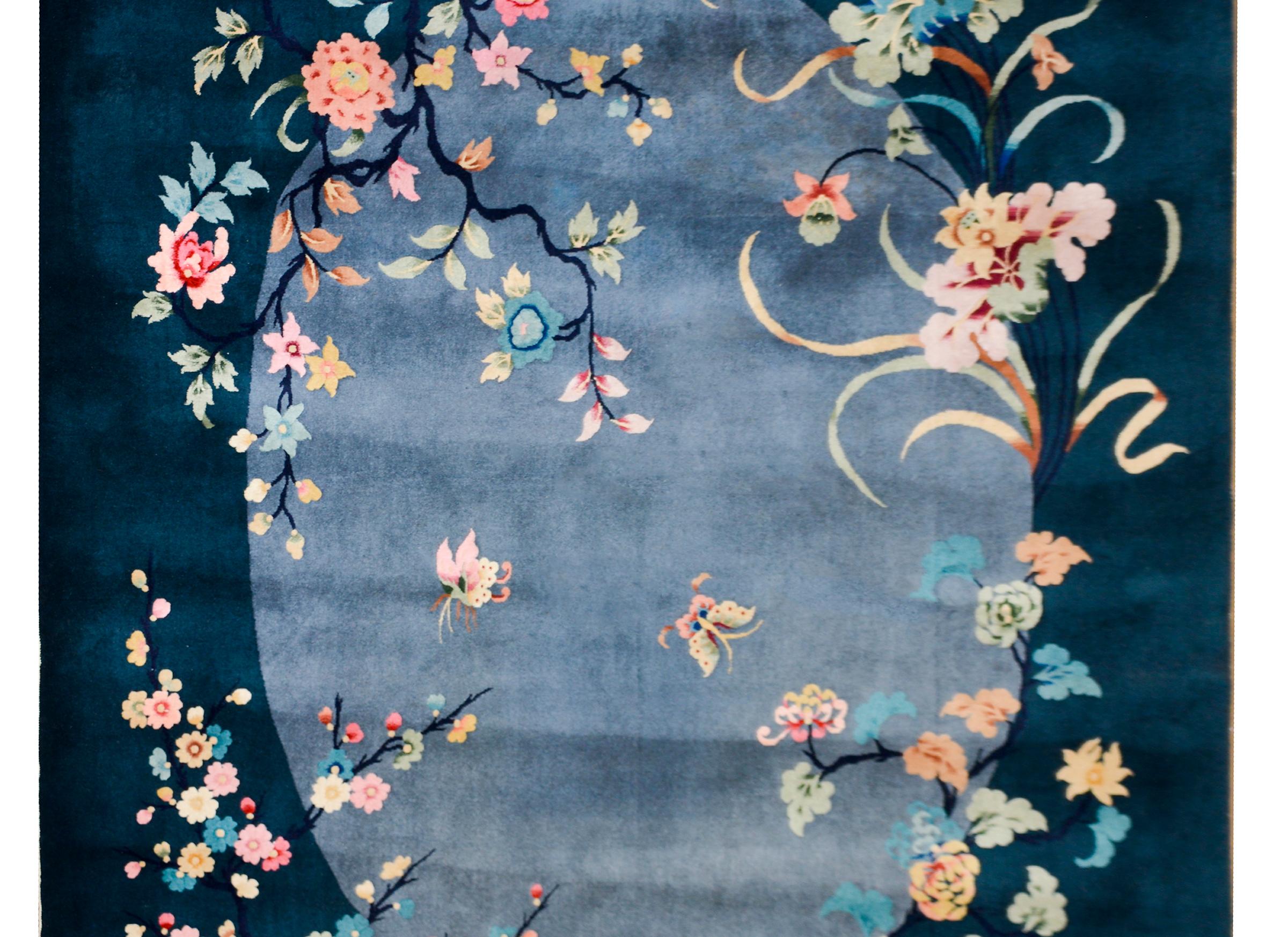 A beautiful early 20th century Chinese Art Deco rug with a dark indigo border surrounded a gray oval medallion overlaid with multi-colored peonies, lotus, chrysanthemum, and sherry blossoms, presenting the four seasons.