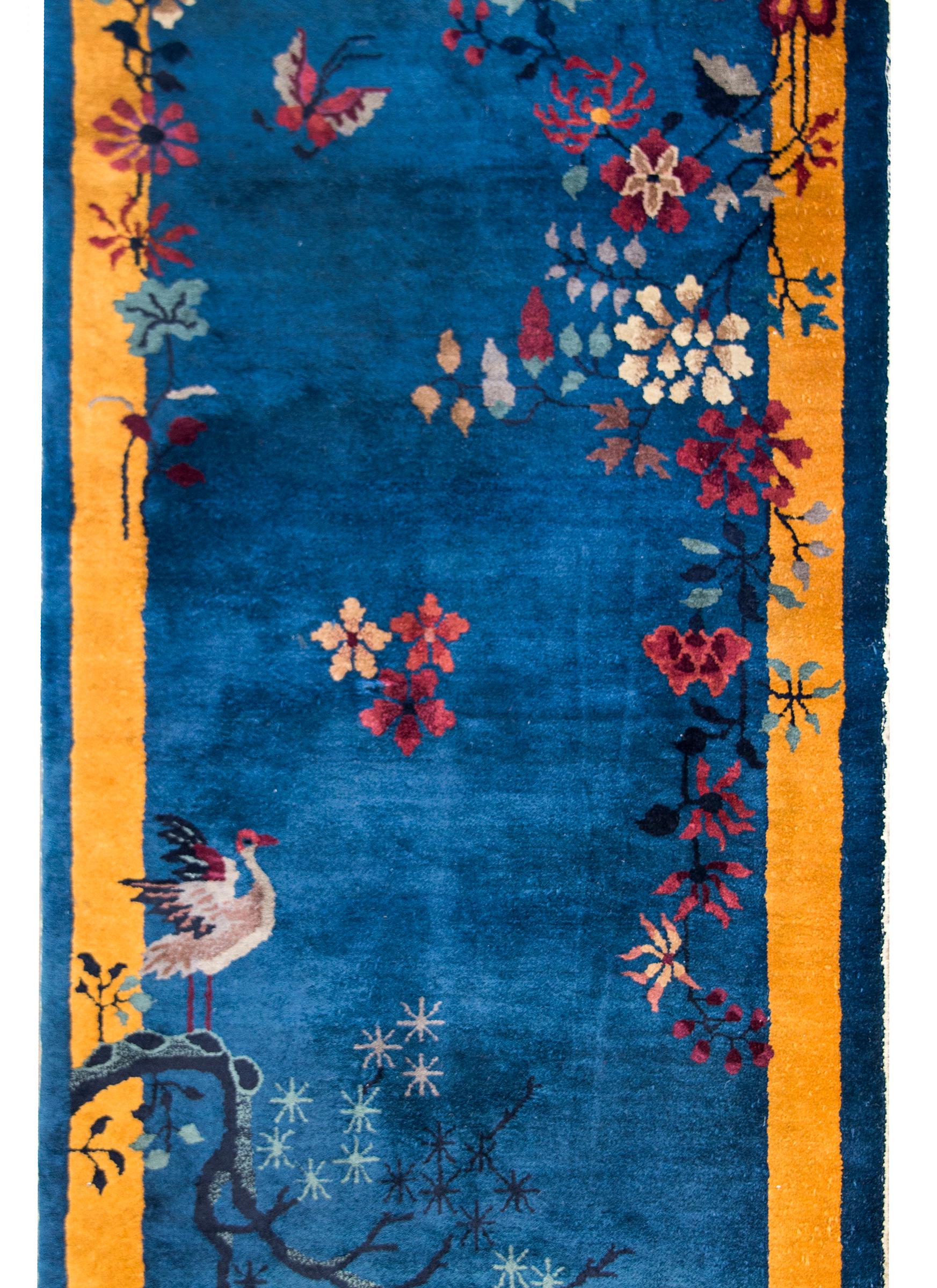 A beautiful early 20th century Chinese Art Deco rug with a brilliant blue field surrounded by a wide gold striped border, and all overlaid with multi-colored peonies, chrysanthemum, and a pine tree with a crane resting on its branch in the lower