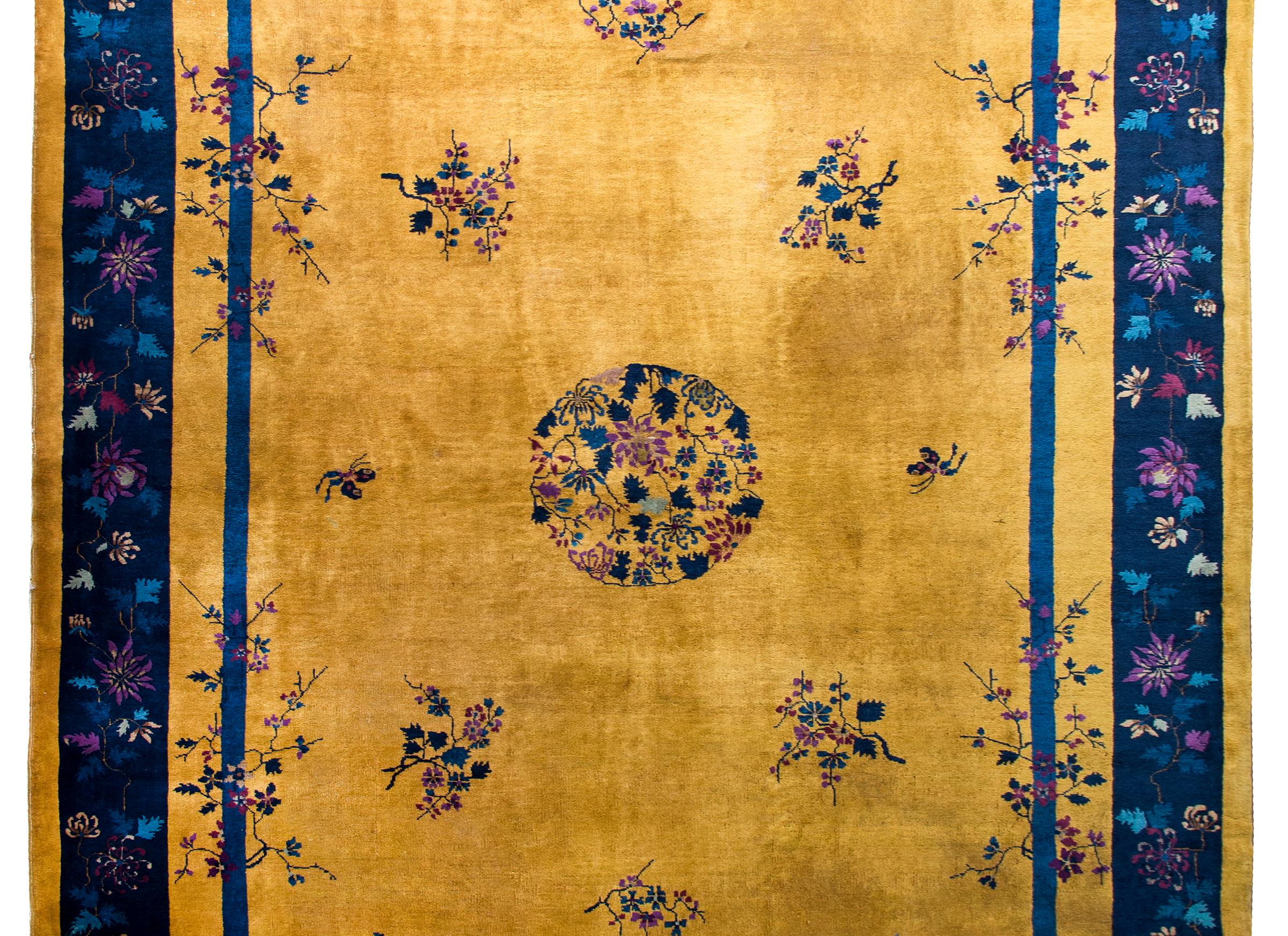 A stunning Chinese Art Deco rug with the most wonderful gold field covered in sprigs of prunus blossoms and a small central chrysanthemum medallion all woven in indigos, violets, and greens. The border is wonderful with a wide indigo striped with a