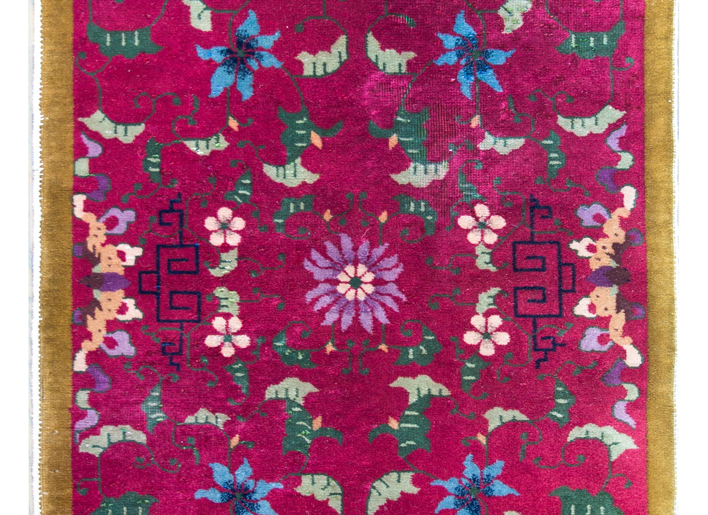 A beautiful early 20th century Chinese Art Deco rug with a central violet chrysanthemum mirrored amidst a mirrored floral and leaf patterned field woven indigo, light and dark green, pink, and orange, and set against a fuchsia background, and