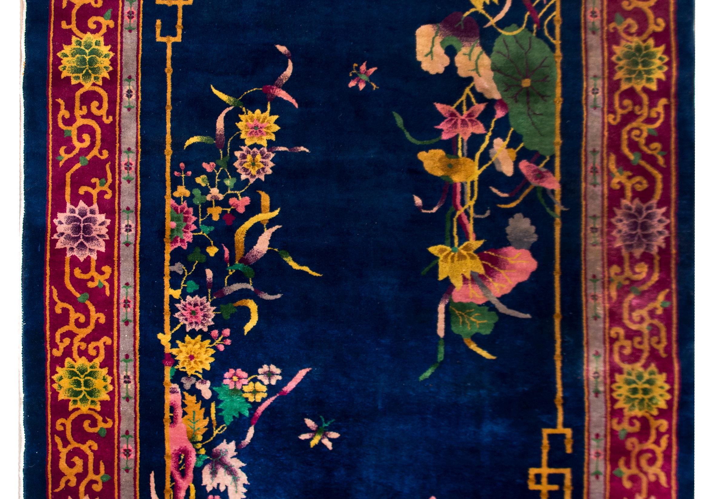 A beautiful early 20th century Chinese Art Deco rug with deep indigo background covered in multi-colored chrysanthemum, peonies, prunus, and lotus blossoms, and surrounded by a wide border with large chrysanthemums and scrolling vines.