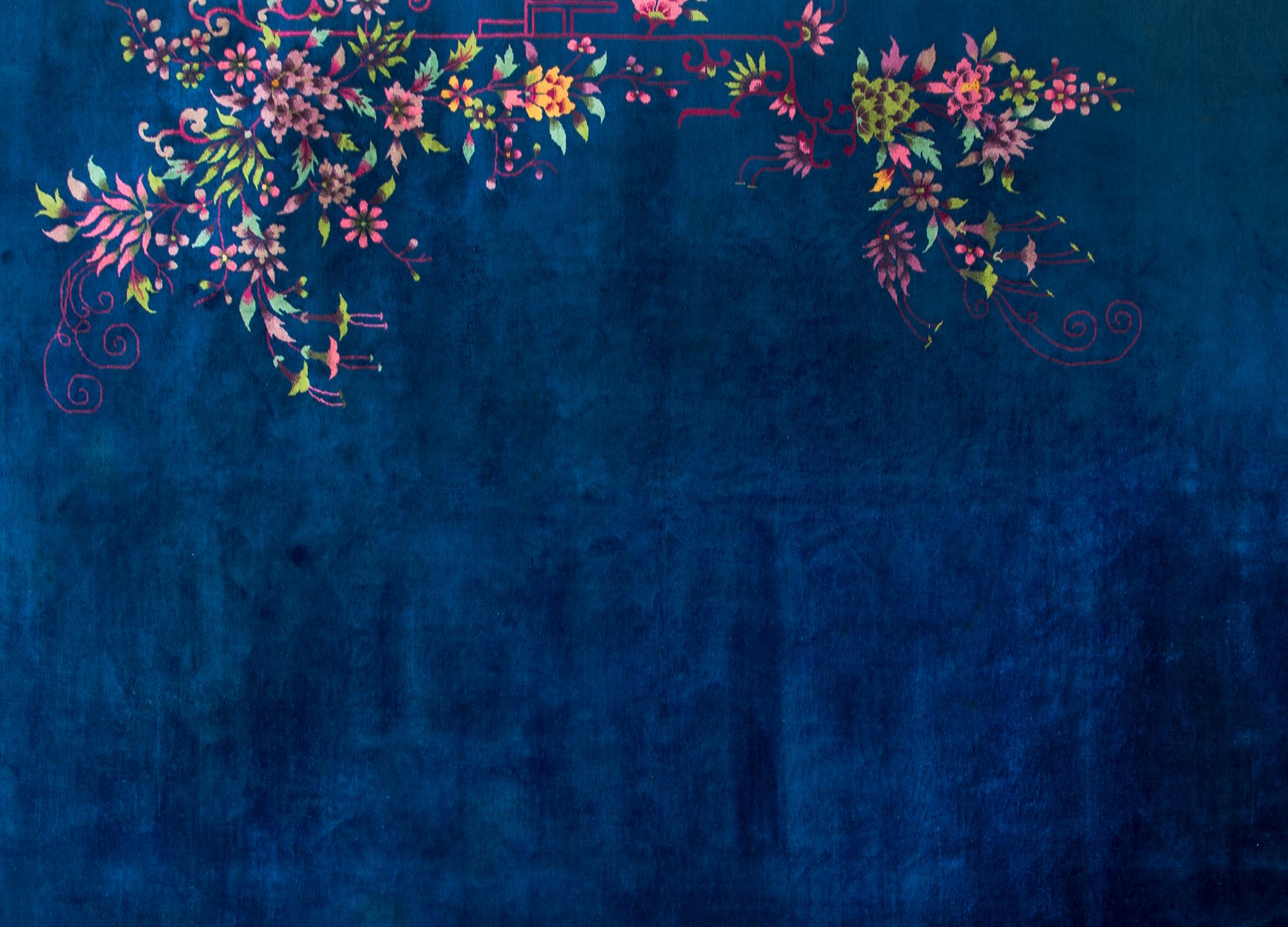 A wonderful early 20th century Chinese Art Deco rug with a bold dark indigo background with an asymmetrical floral cluster with chrysanthemums, peonies, and prunus blossoms woven in myriad colors including pinks, oranges, turquoises, and greens.