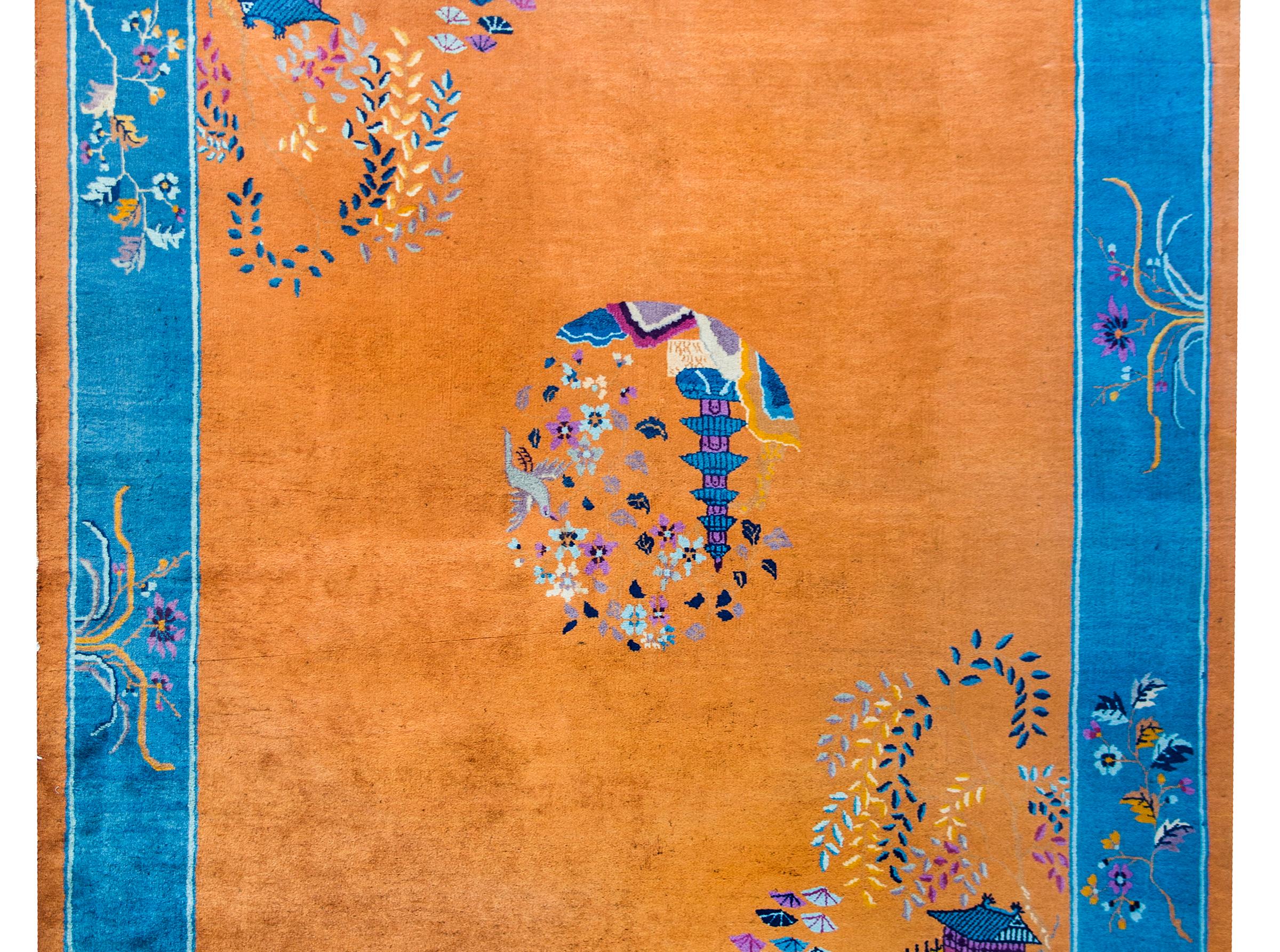 A beautiful early 20th century Chinese Art Deco rug with a dark golden orange field with a central pagoda medallion, garden pavilions in opposite corners, and surrounded by a wide indigo border overlaid with peonies, chrysanthemum, and other