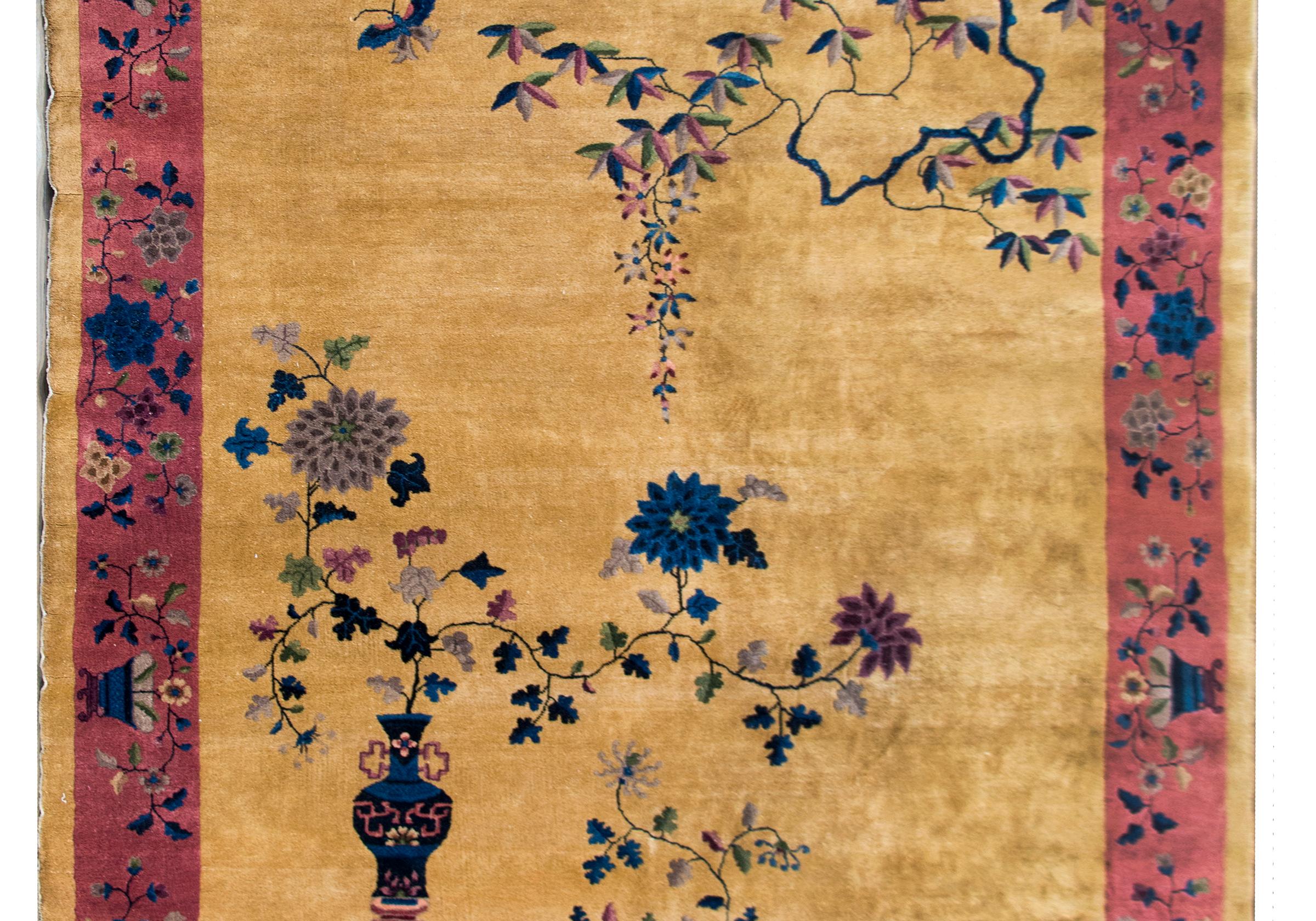 A wonderful early 20th century Chinese Art Deco rug with a rich gold field surrounded by a wide cranberry field and all overlaid with myriad auspicious flowers including chrysanthemums, peonies, cherry blossoms, and gnarly hysteria vines, all woven