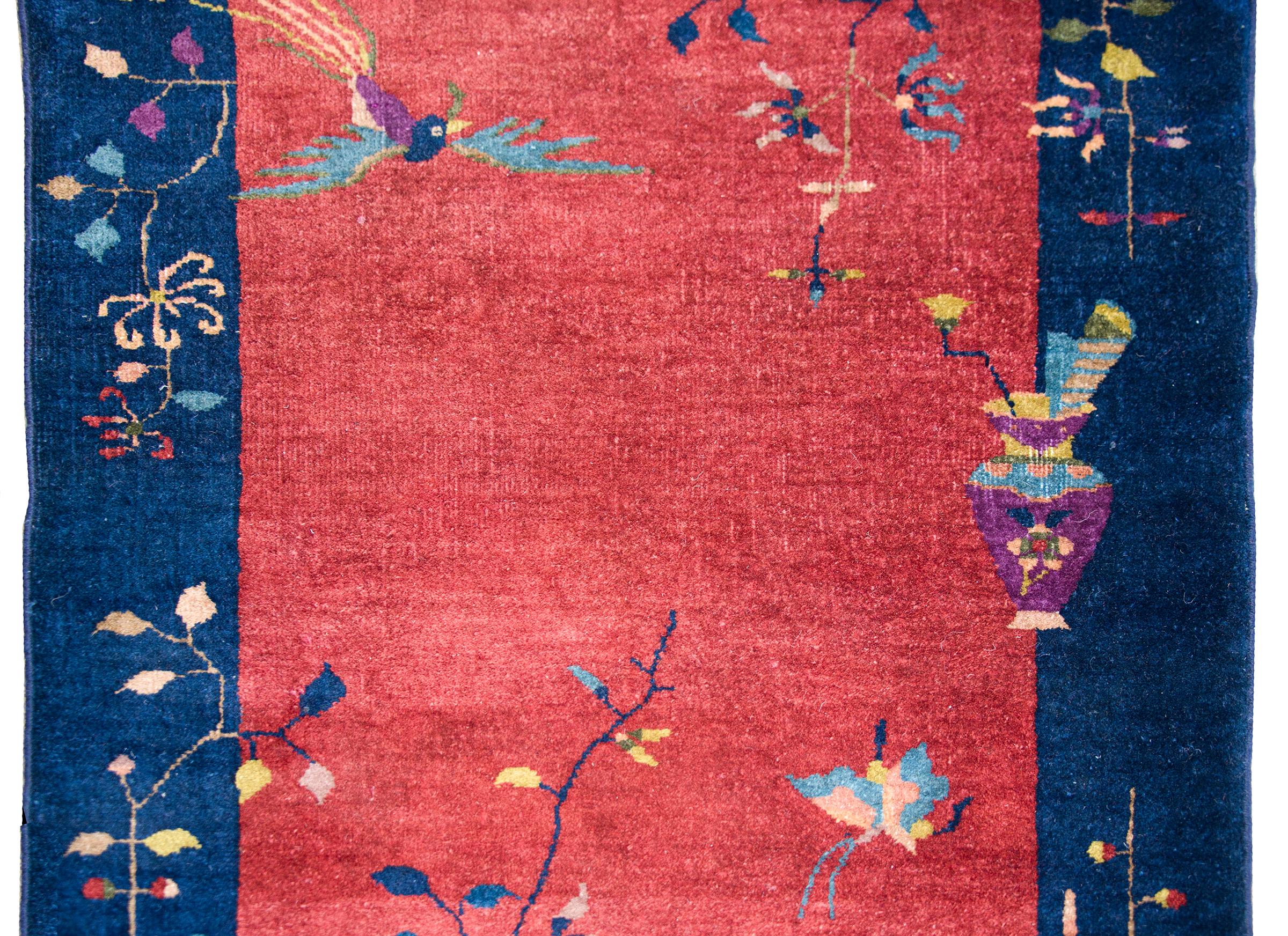 A wonderful early 20th century Chinese Art Deco rug with a cranberry field surrounded by a wide indigo border, and all overlaid with multi-colored auspicious flowers including peonies, chrysanthemum, and cherry blossoms, with with a scholar's vase,