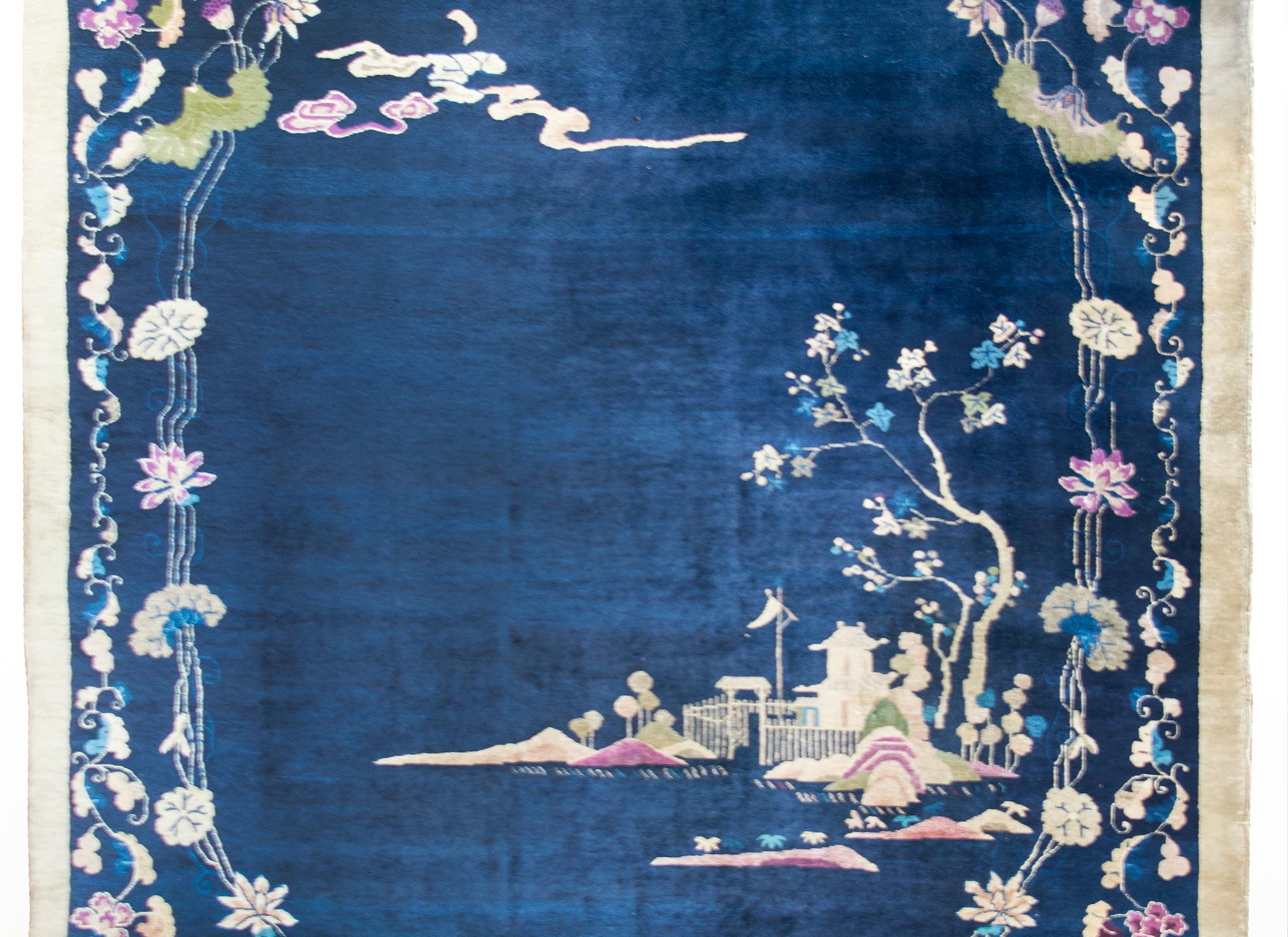 A wonderful early 20th century Chinese Art Deco rug with a dark indigo field surrounded by a lacy floral and scrolling vine border with an oval cutout framing a garden landscape with pavilion and mountainous landscape, and all woven in beautiful