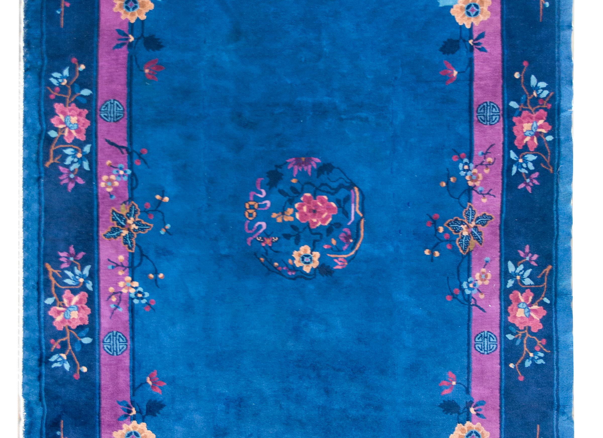 An early 20th century Chinese Art Deco rug with a central floral medallion with pink and fuchsia peonies, set against an indigo background, and surrounded by a wide border with a repeated peony pattern with Shou characters, a symbol is prosperity in