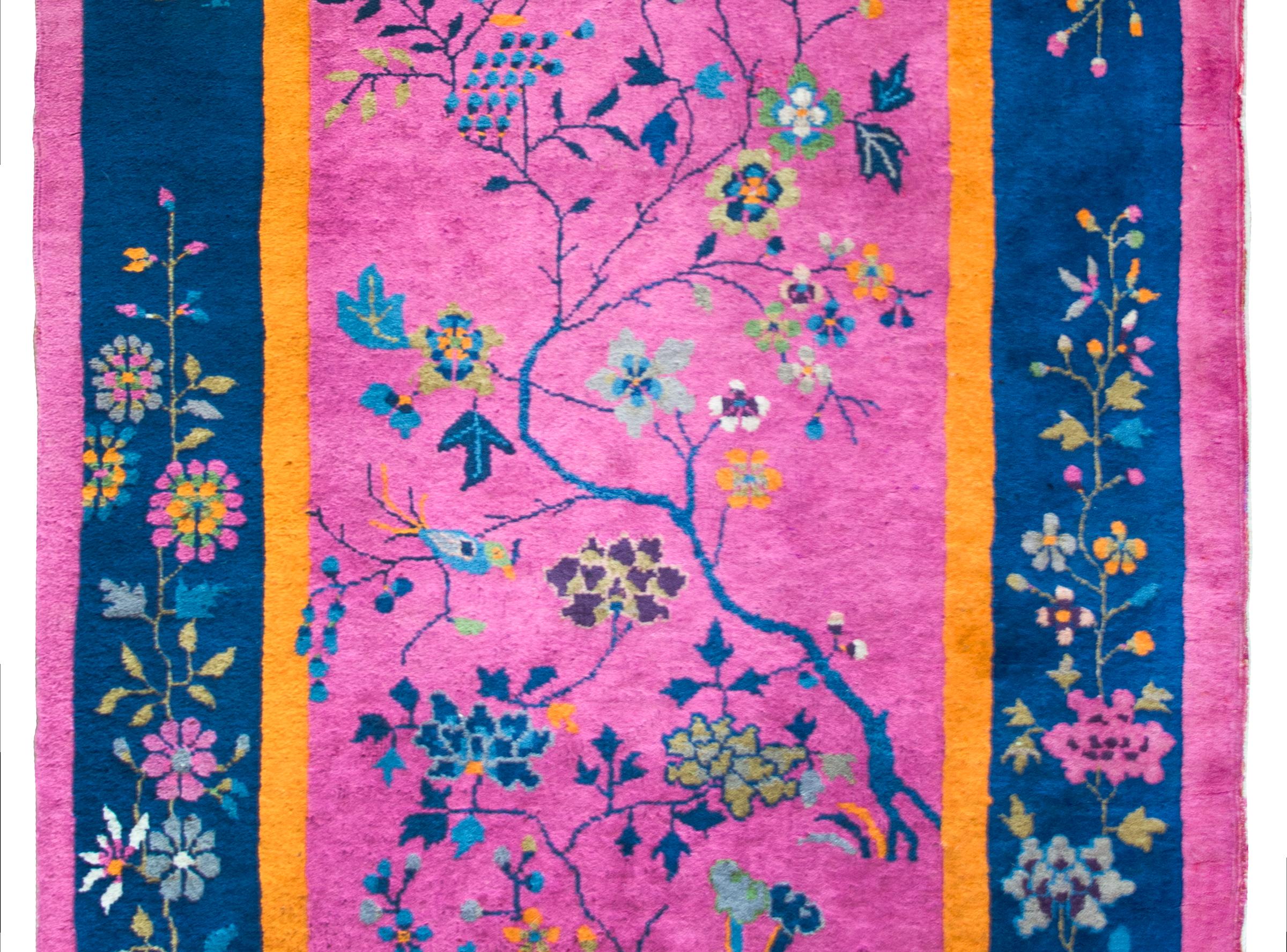 A wonderful early 20th century Chinese Art Deco rug with a brilliant fuchsia field surrounded by thin orange, wide indigo, and thin fuchsia borders, and all overlaid with multi-colored branches with hanging grape clusters, peonies, and cherry