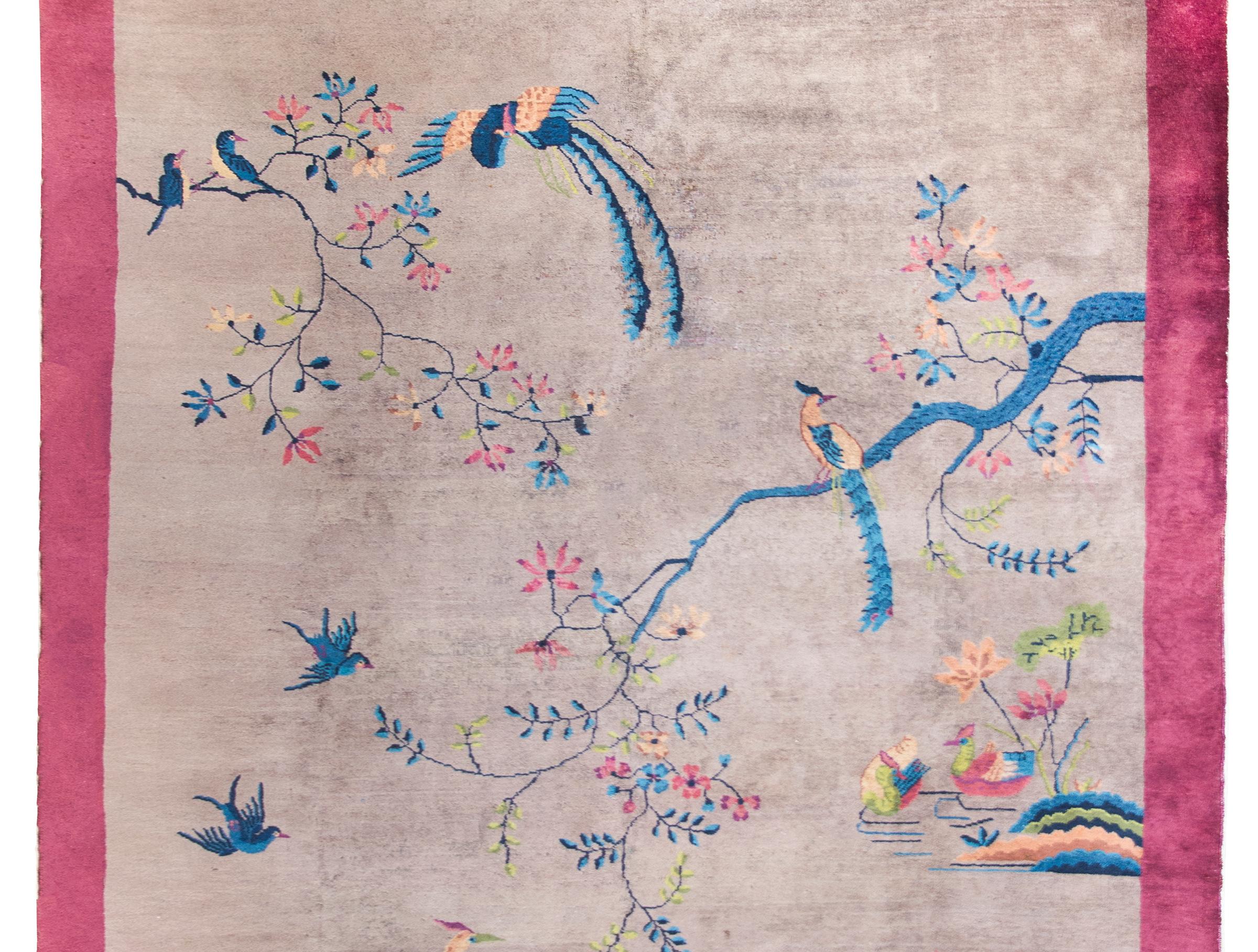 A beautiful early 20th century Chinese Art Deco rug with a gray field surrounded by a wide eggplant colored border, and the central field overlaid with a garden landscape image including multi-colored flowering branches, phoenix and magpies flying