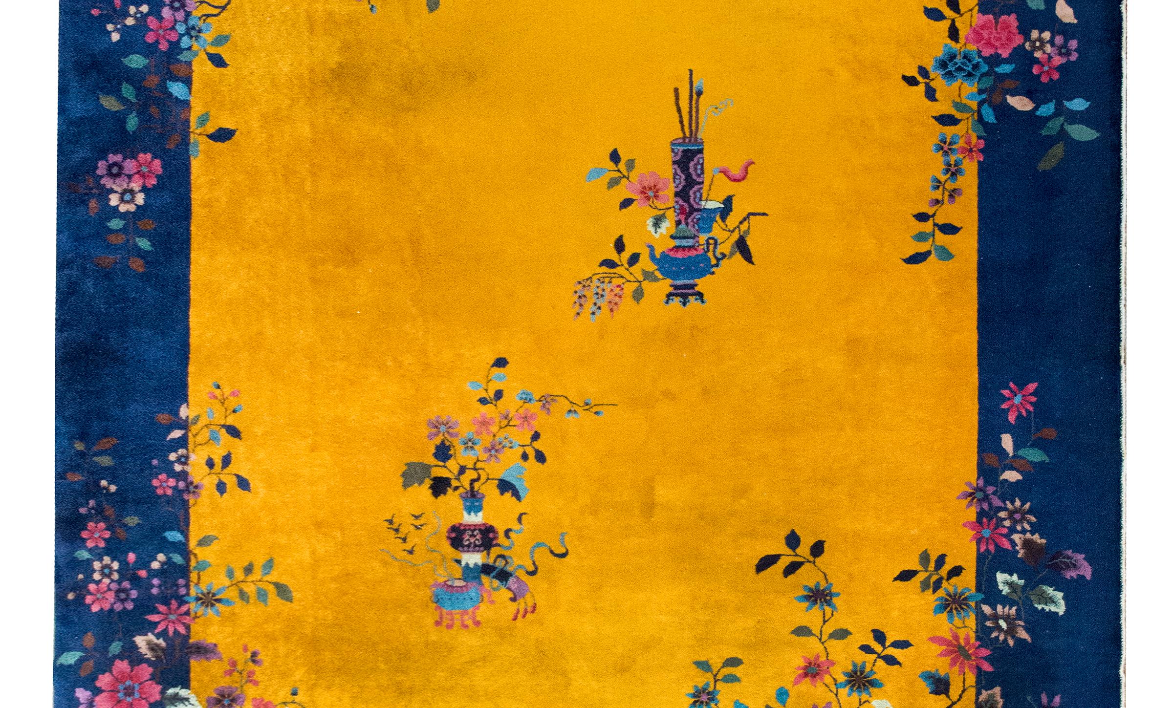 A wonderful and brilliant early 20th century Chinese Art Deco rug with a brilliant gold central field surrounded by a wide indigo border, and all overlaid with myriad flowers including peonies, cherry blossoms, wisteria, and chrysanthemums, and all