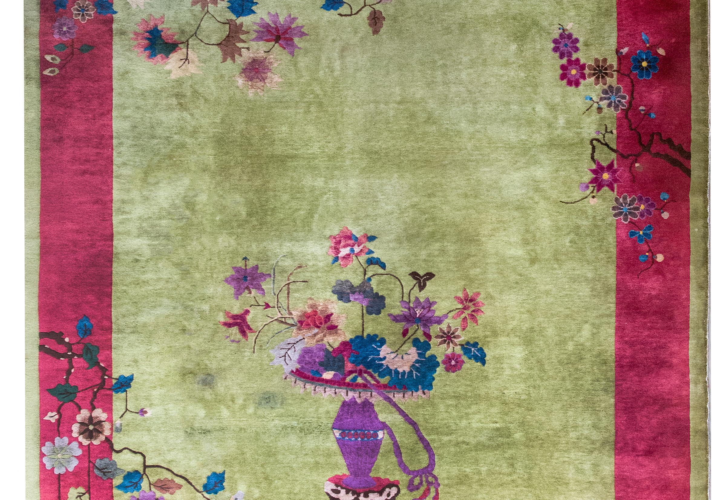 An early 20th century Chinese Art Deco rug with a rare and wonderful lime green background surrounded by a wide cranberry border, and all overlaid with myriad auspicious flowers including peonies, chrysanthemums, and cherry blossoms, and all woven