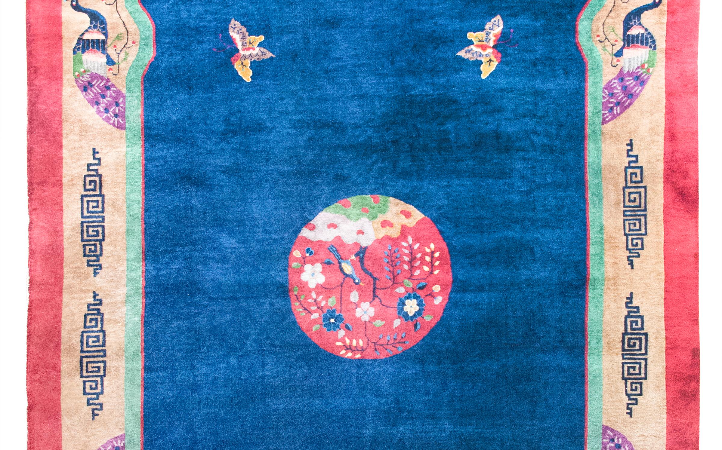 Remarquable tapis chinois Art déco du début du XXe siècle. Le médaillon central représente un oiseau assis sur une pivoine et flottant dans un champ indigo avec quatre papillons (symboles de bonne fortune), le tout entouré d'une magnifique bordure