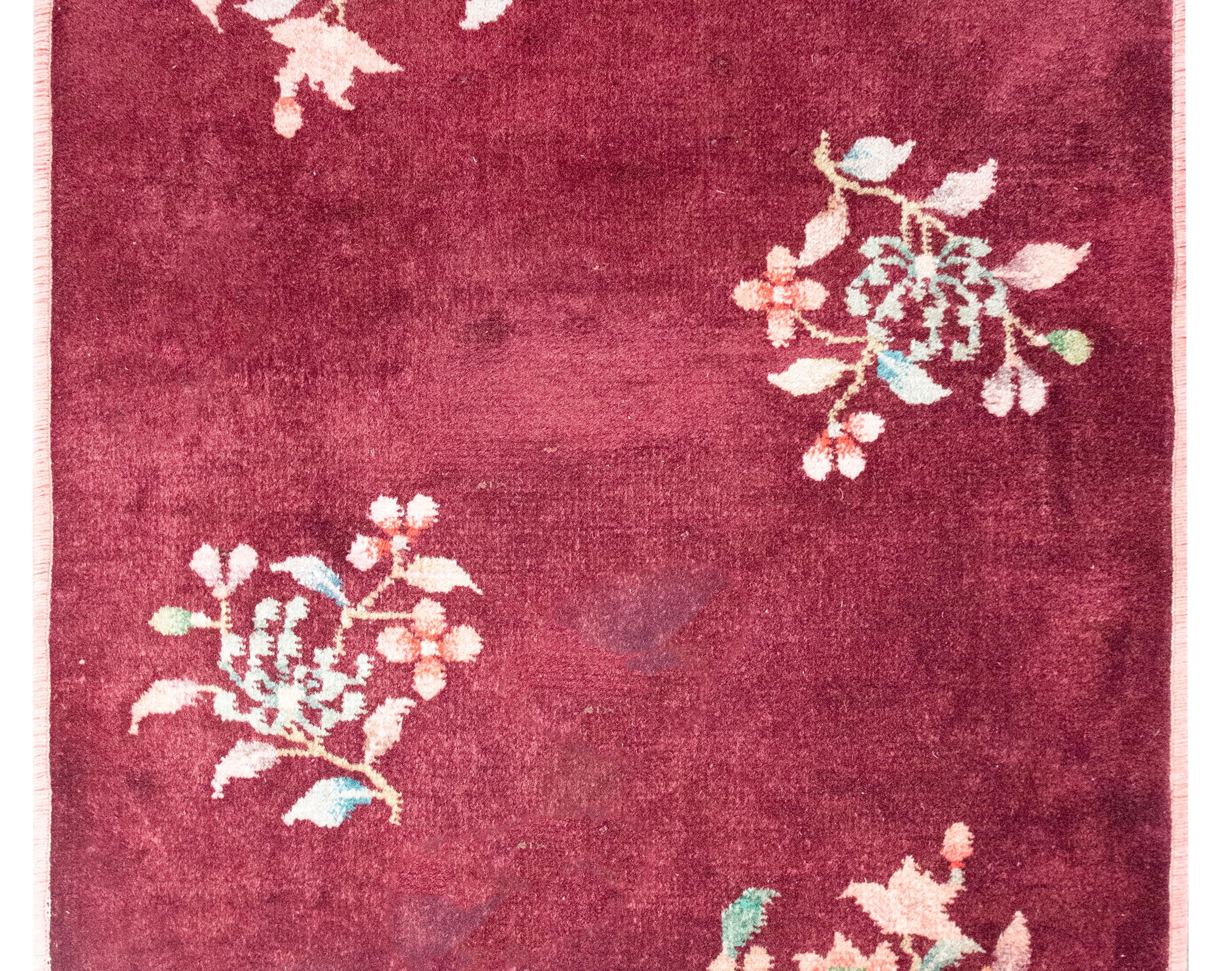 A stunning early 20th century petite Chinese Art Deco rug with a cranberry field with two chrysanthemum clusters in opposing corner, and two cherry blossoms clusters on the center, and all woven in pastel pinks, greens, yellow, and indigos.  