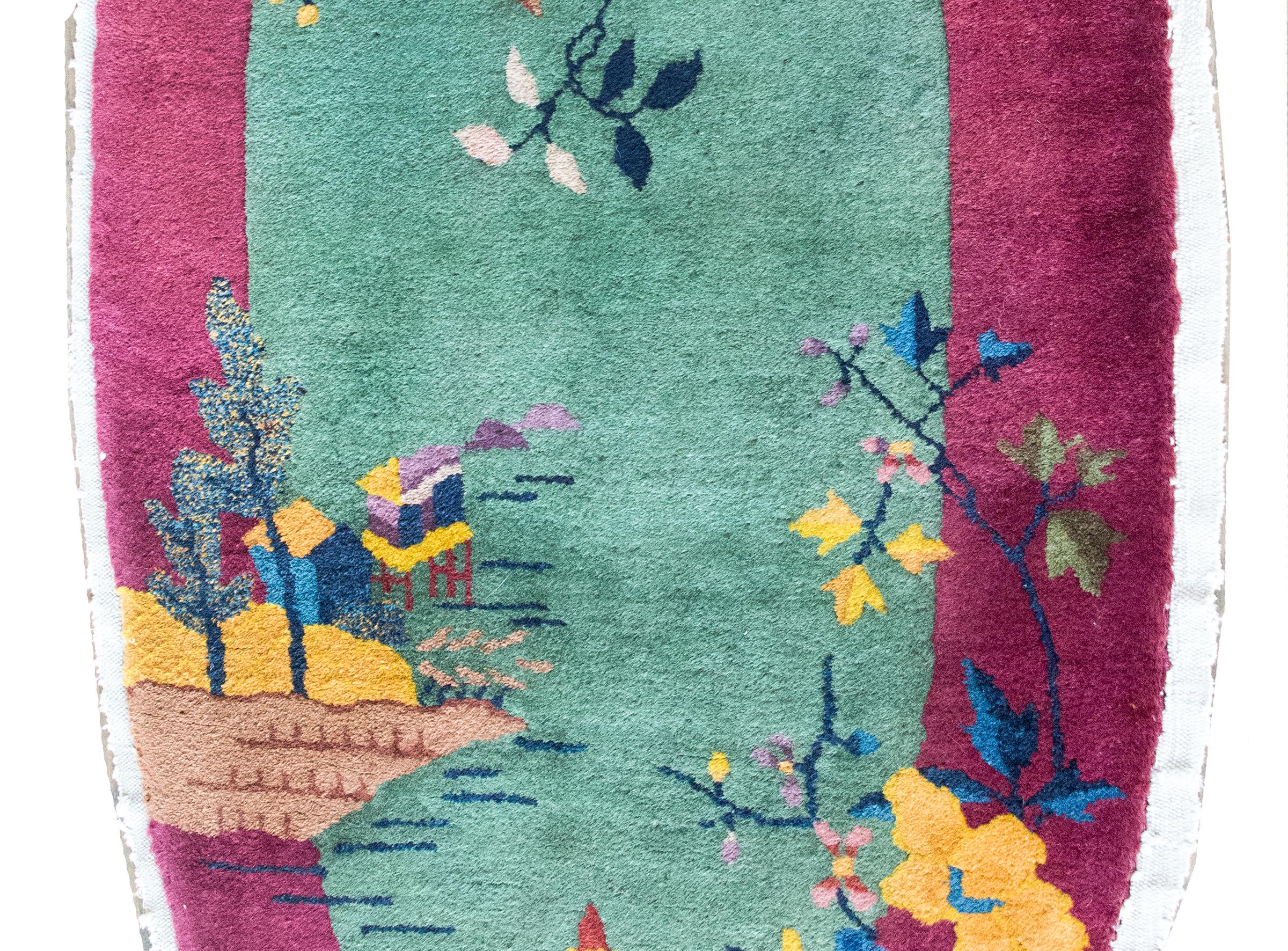 Charmant petit tapis ovale Art déco chinois du début du 20e siècle, avec un champ vert entouré d'une large bordure violette, le tout recouvert d'une scène de paysage de jardin comprenant une pagode et un pavillon de jardin au bord d'un étang, avec