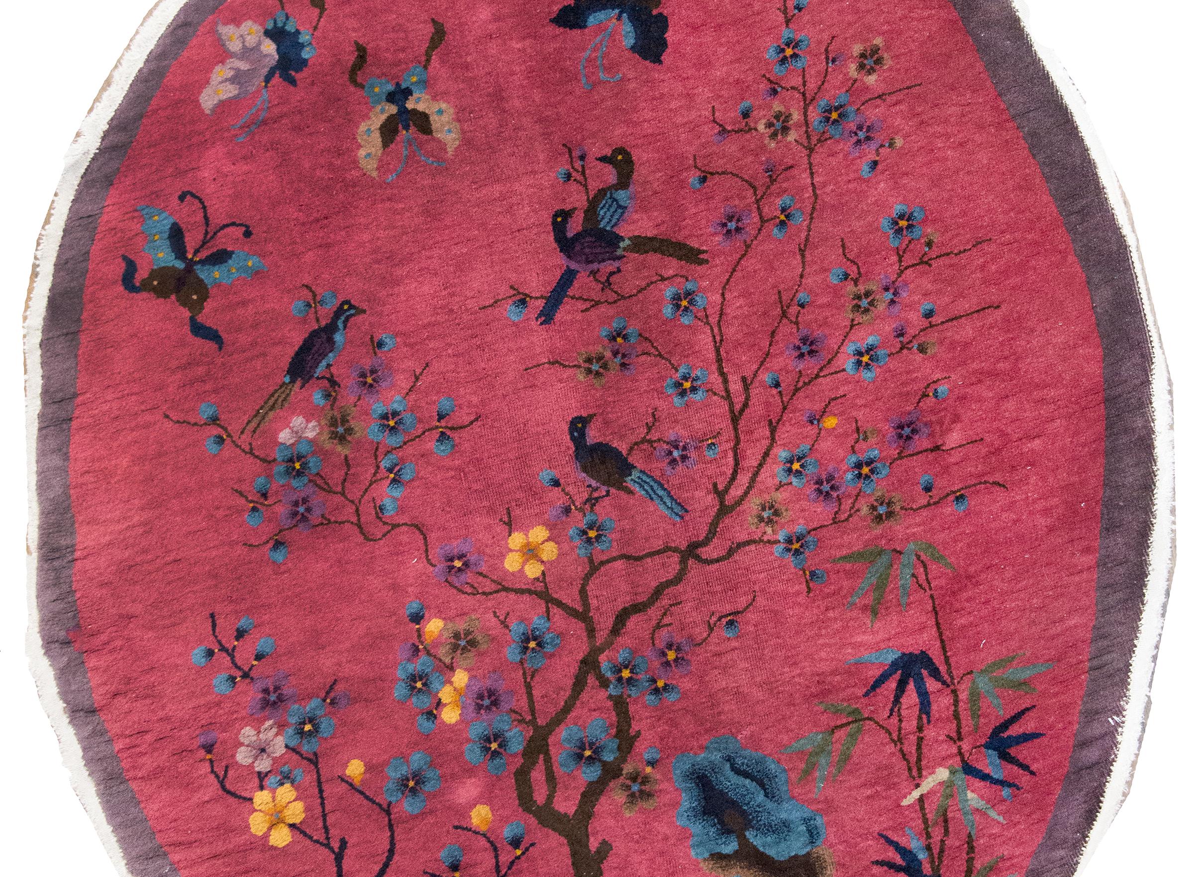Remarquable tapis ovale de style Art déco chinois du début du XXe siècle, tissé avec un motif riche et symbolique. En son cœur, un cerisier en fleurs gracieusement arqué émerge des rochers des érudits, ses branches délicates étant animées par quatre