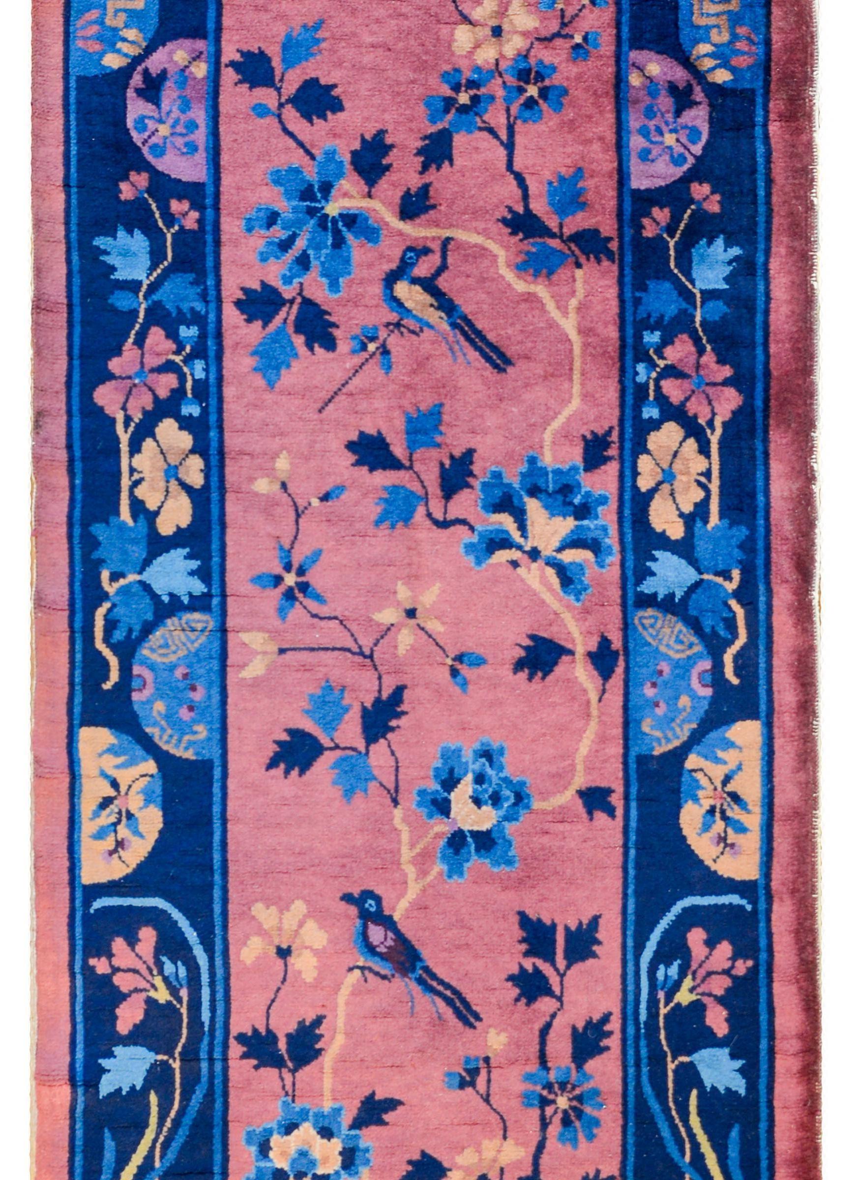 An early 20th century Chinese Art Deco runner with a mauve colored field with a beautiful pattern of flowering peonies and prunus blossoms on scrolling branches with magpies, all rendered in light and dark indigo with beige and violet. The border is