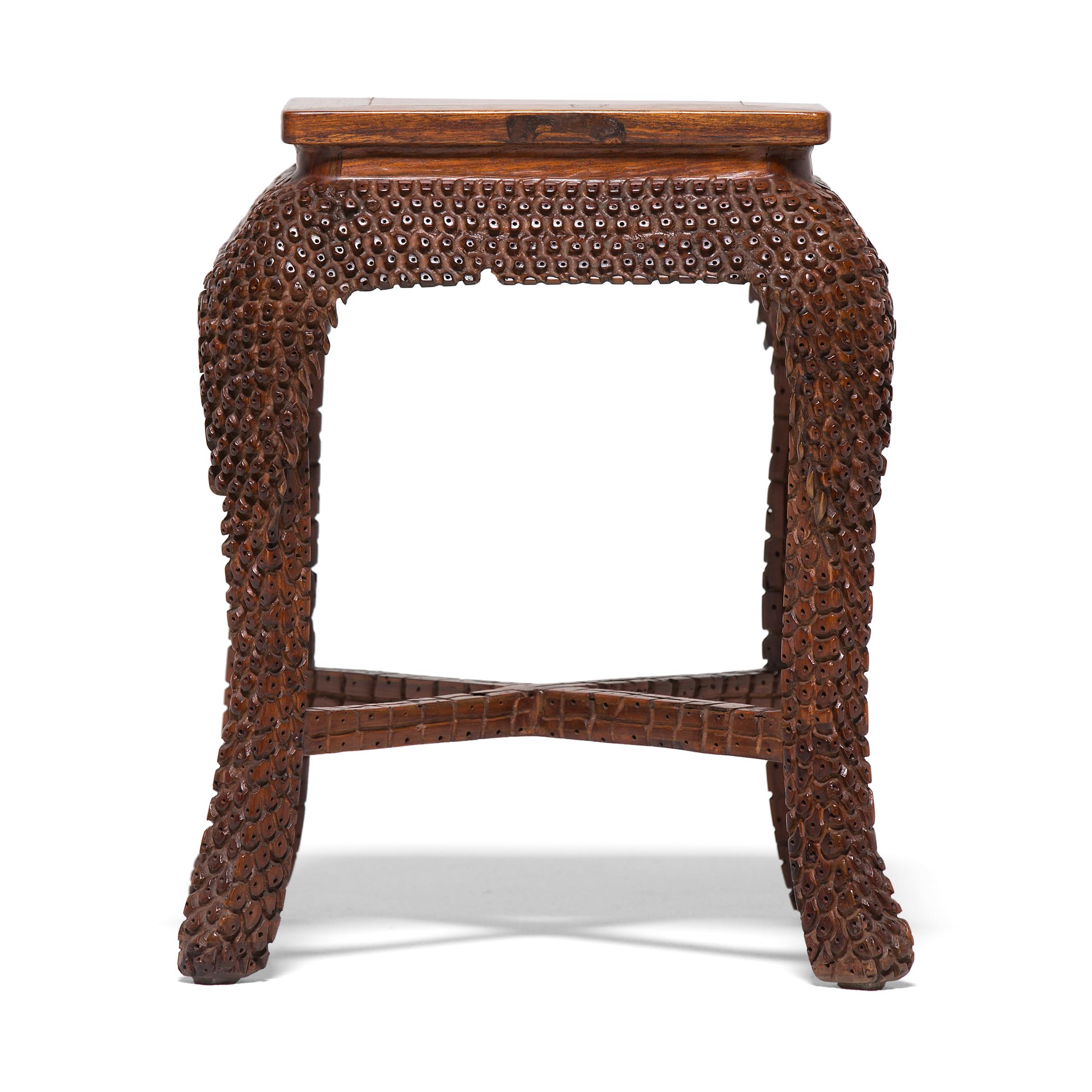 This early 20th century stool from Beijing, China was crafted from a fine hardwood with beautiful warm coloring and tight grain. Intricate carvings cover the stool's frame, patterning the legs and apron 