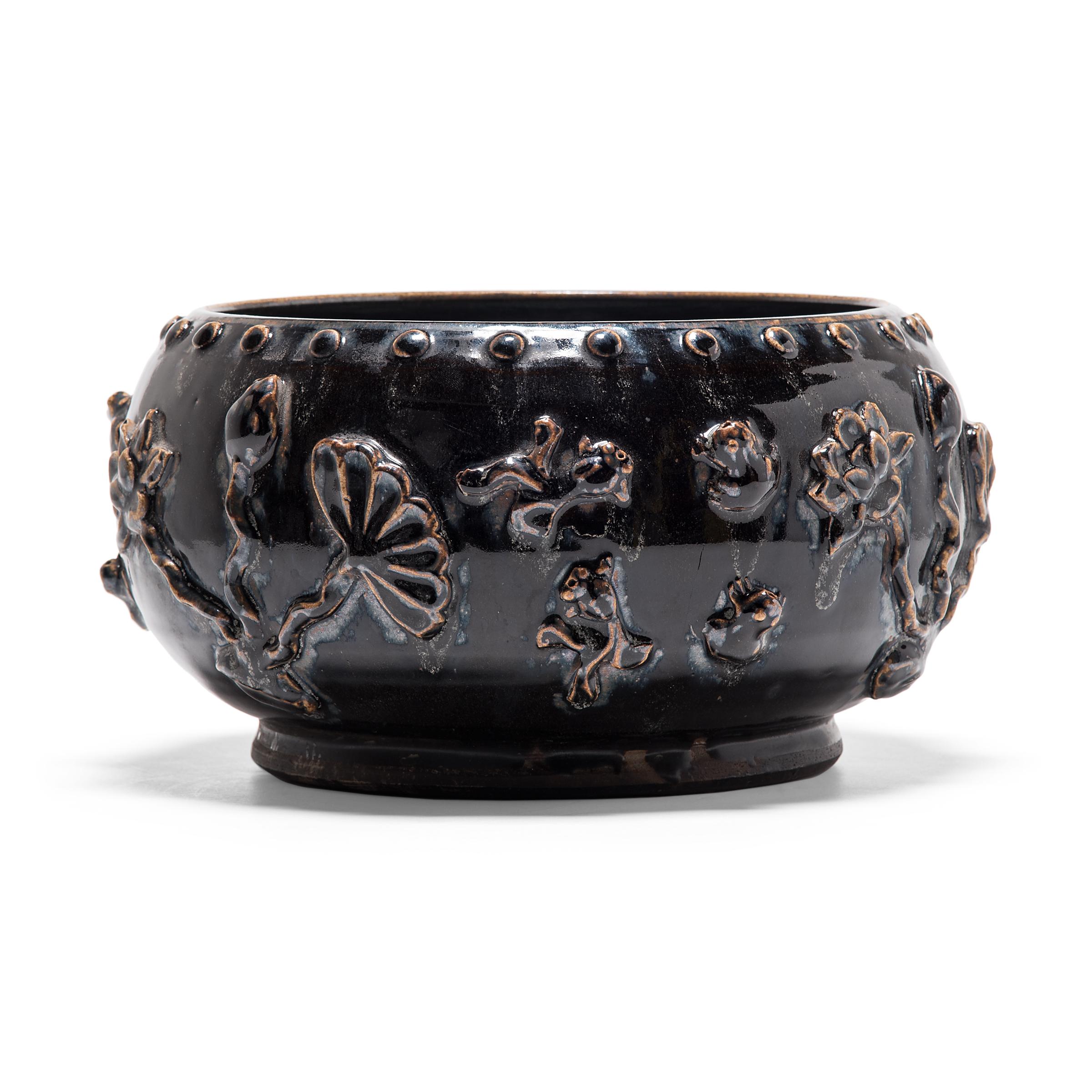 A dark, glossy glaze sheets, pools, and drips down the surface of this squat early 20th century vessel, lingering beautifully on every imperfection. Sculpted in China's Shanxi province, the footed bowl is patterned with a band of nailhead and