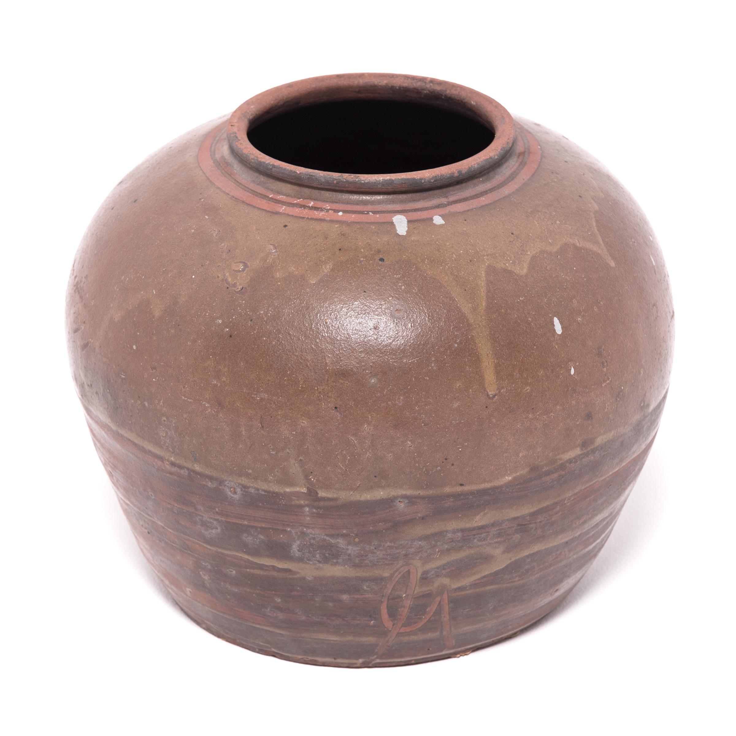 Tracing its roots back into the Han dynasty, this early 20th-century vessel emulates the full-bodied shapes and unusual glazing found in ancient ceramics. Marked with barren spots, a greenish brown glaze clings to the pot’s broad shoulders, dripping
