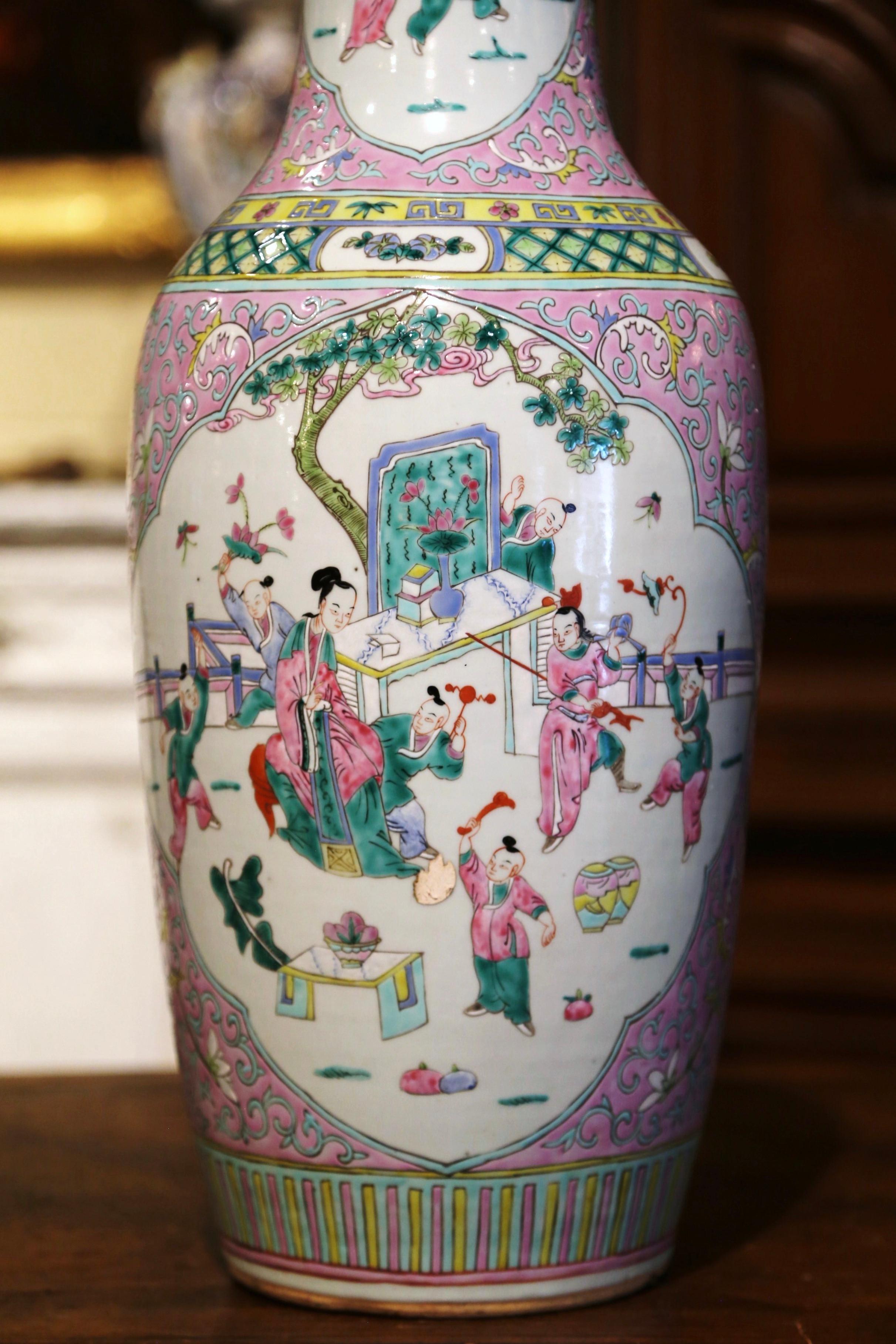 Crafted in China circa 1920, the tall vase is round in shaped with an elegant long neck. The colorful antique urn is decorated with hand painted figural motifs including a mother playing with children. The large Famille Rose vessel is in excellent
