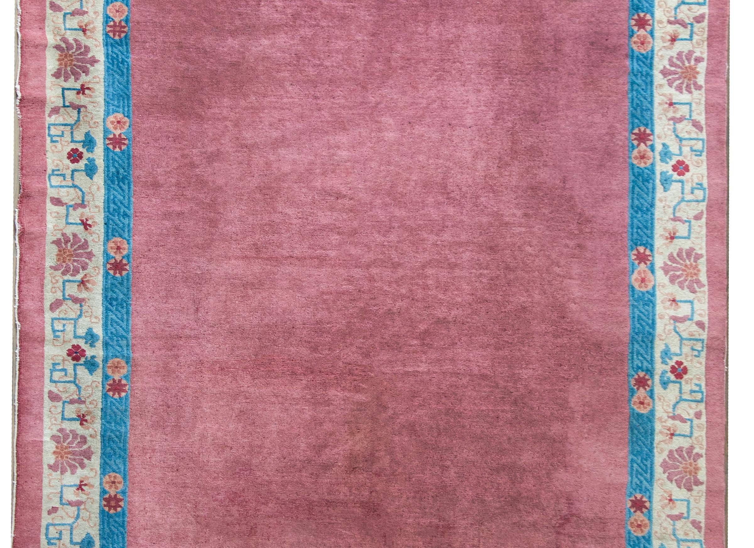 A wonderful early 20th century Chinese Feti rug with a solid mauve central field surrounded by a border with an indigo meandering motif and repeated floral inner stripe and a wide repeated floral and stylized scrolling dragon outer border.
