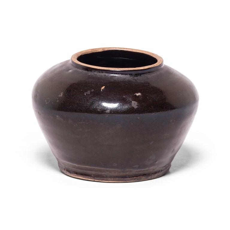 A thick dark glaze clings to the smooth surface of this petite jar, lingering on imperfections and accentuating the subtle ridges of its tapered form. Crafted in the late 19th century, the wide-mouth jar was once used to store food in a Qing-dynasty