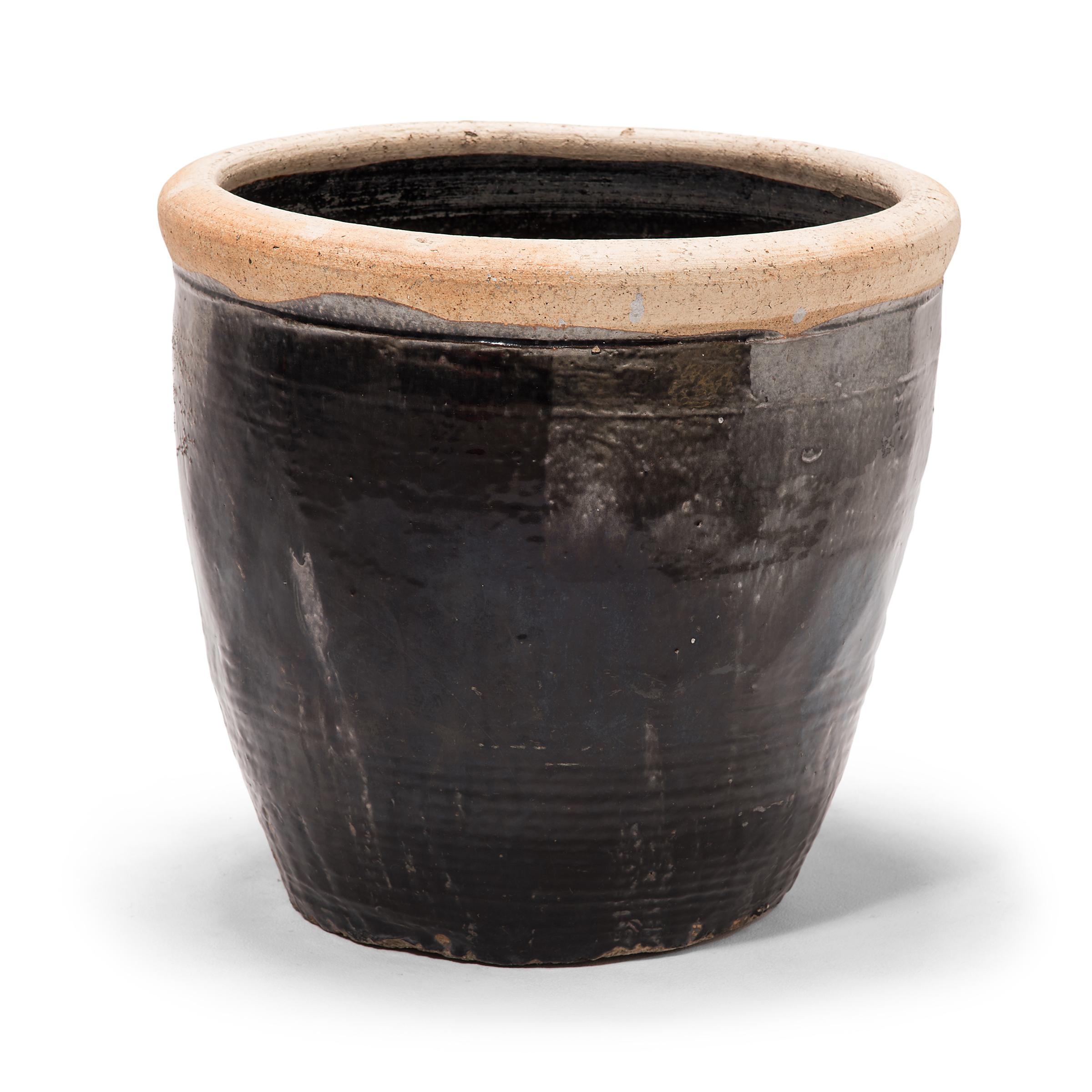 Originally used for pickling foods, this early 20th century vessel is coated inside and out with a dark glaze. Subtle ridges at the base suggest that the wide jar was fashioned by coiling flattened ropes of clay into the desired shape. Featuring an