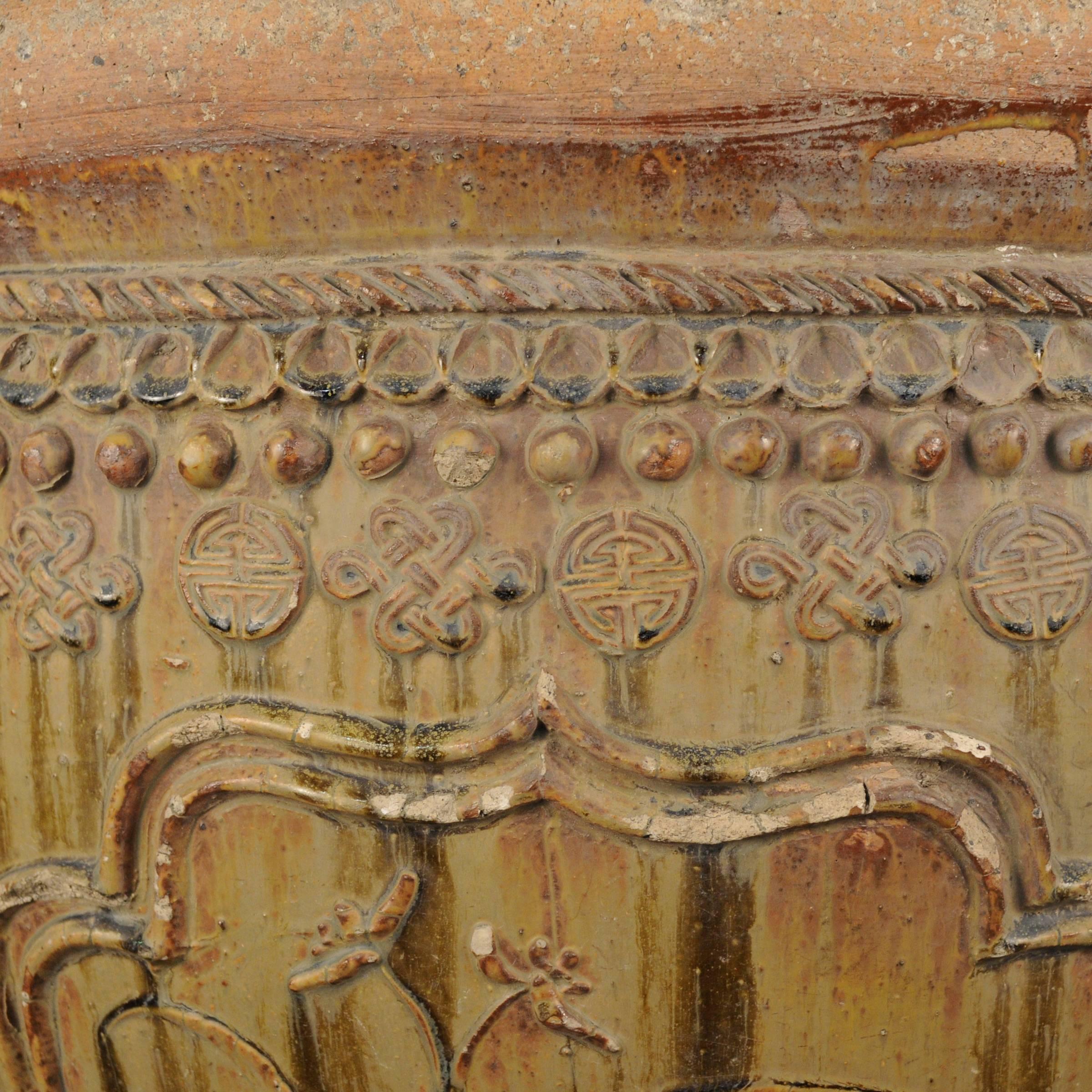 Ce récipient en céramique de grande taille a été fabriqué à la main dans le nord de la Chine au début du XXe siècle. Il est orné d'un haut-relief de médaillons encadrant des motifs floraux. Bordé de textures, le vase est recouvert à l'intérieur et à