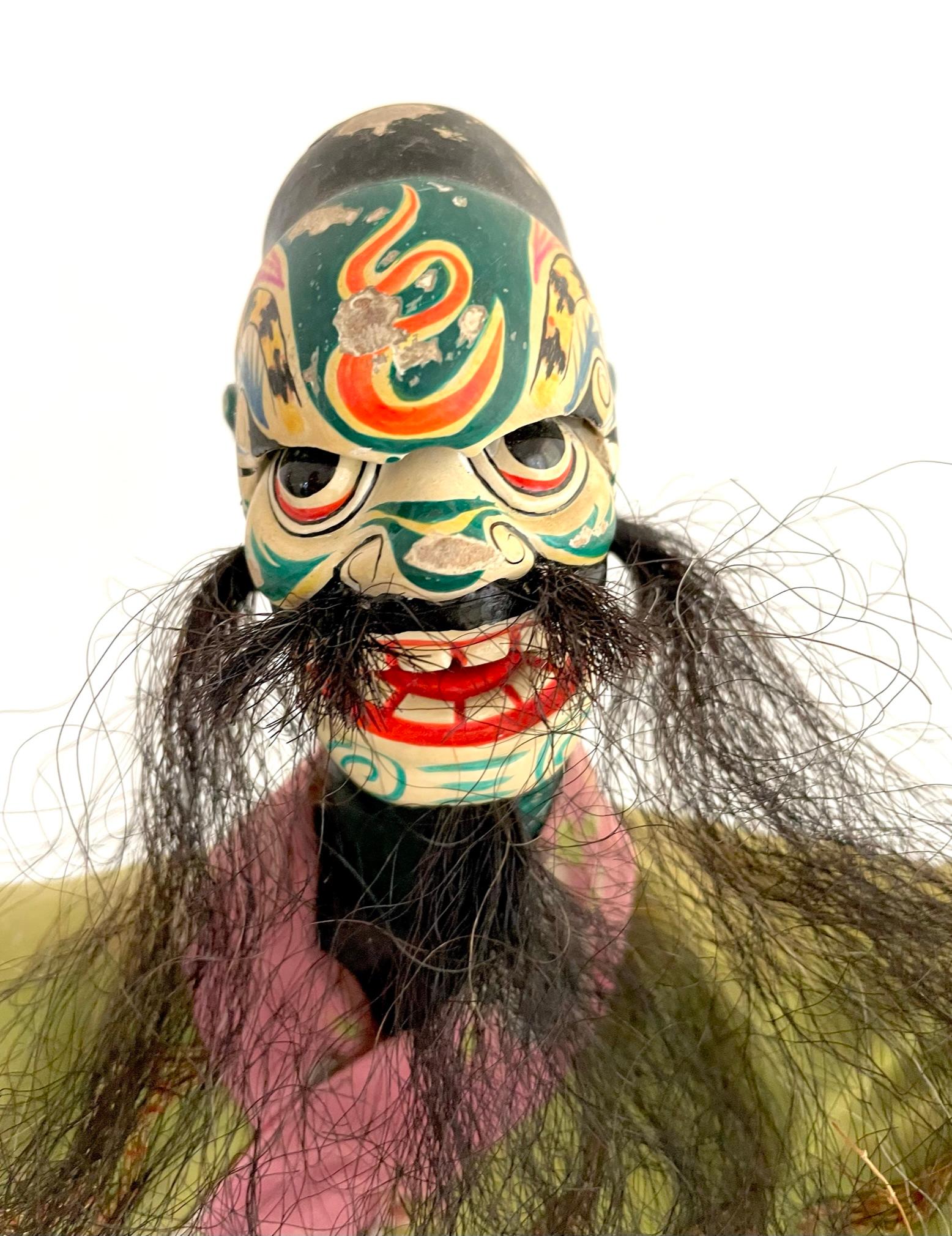 This Chinese opera hand puppet is dress in an elegant, embroidered silk dragon robe. The puppet head is of painted wood. The white face usually represents a villain. Puppetry is a major entertainment performance art in Chinese traditional theatre.