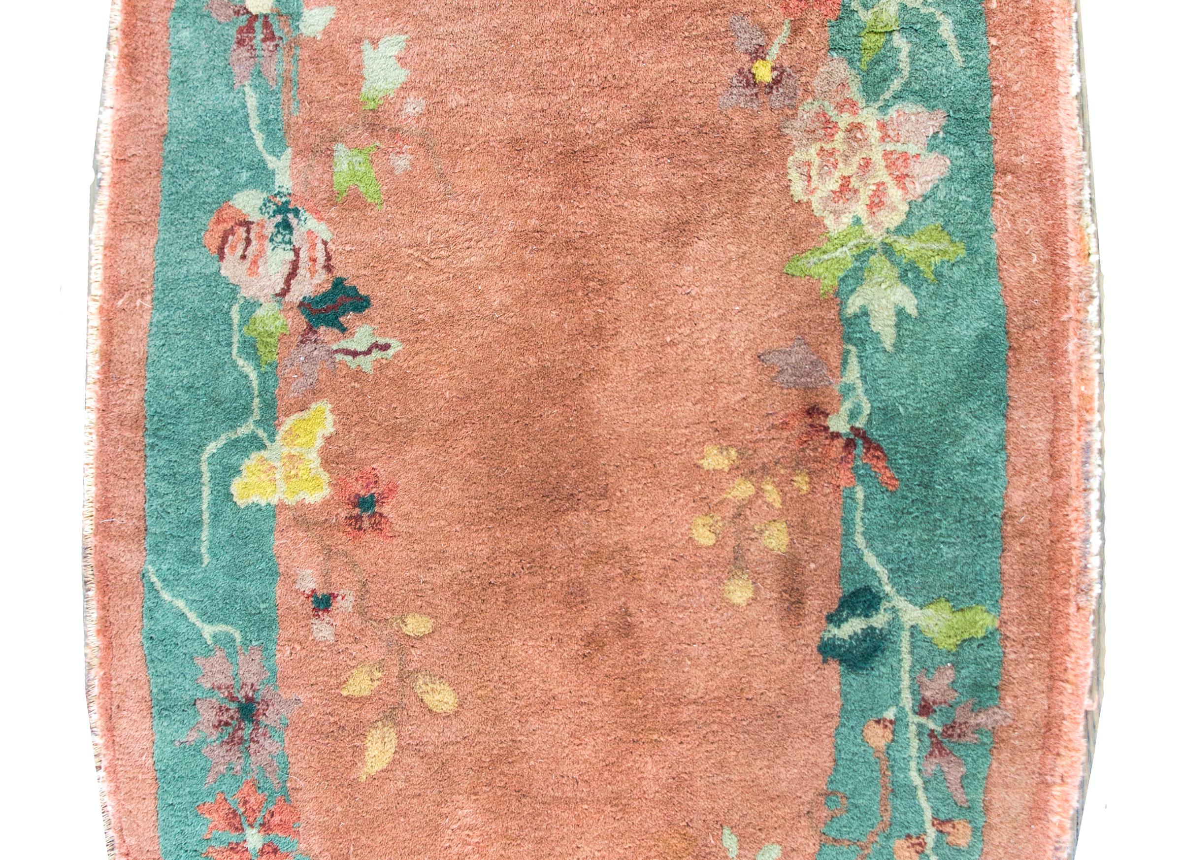 A sweet early 20th century oval Chinese Art Deco rug with a peach central field surrounded by a teal and peach border overlaid with multi-colored peonies, cherry blossoms, lotus, and chrysanthemums.  