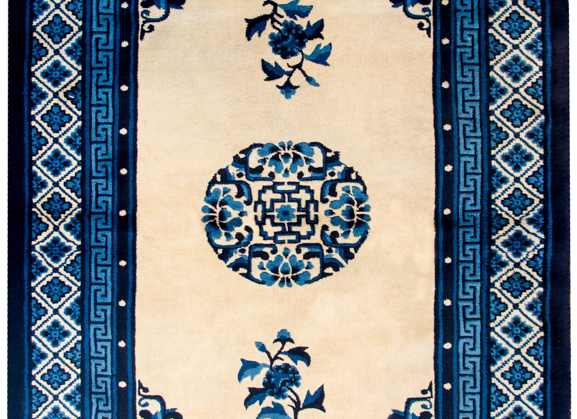 An early 20th century Chinese Peking rug with a large round central floral medallion flanked by two blossoming peonies on a beautiful champagne colored ground surrounded by multiple varying shades of indigo borders.
 