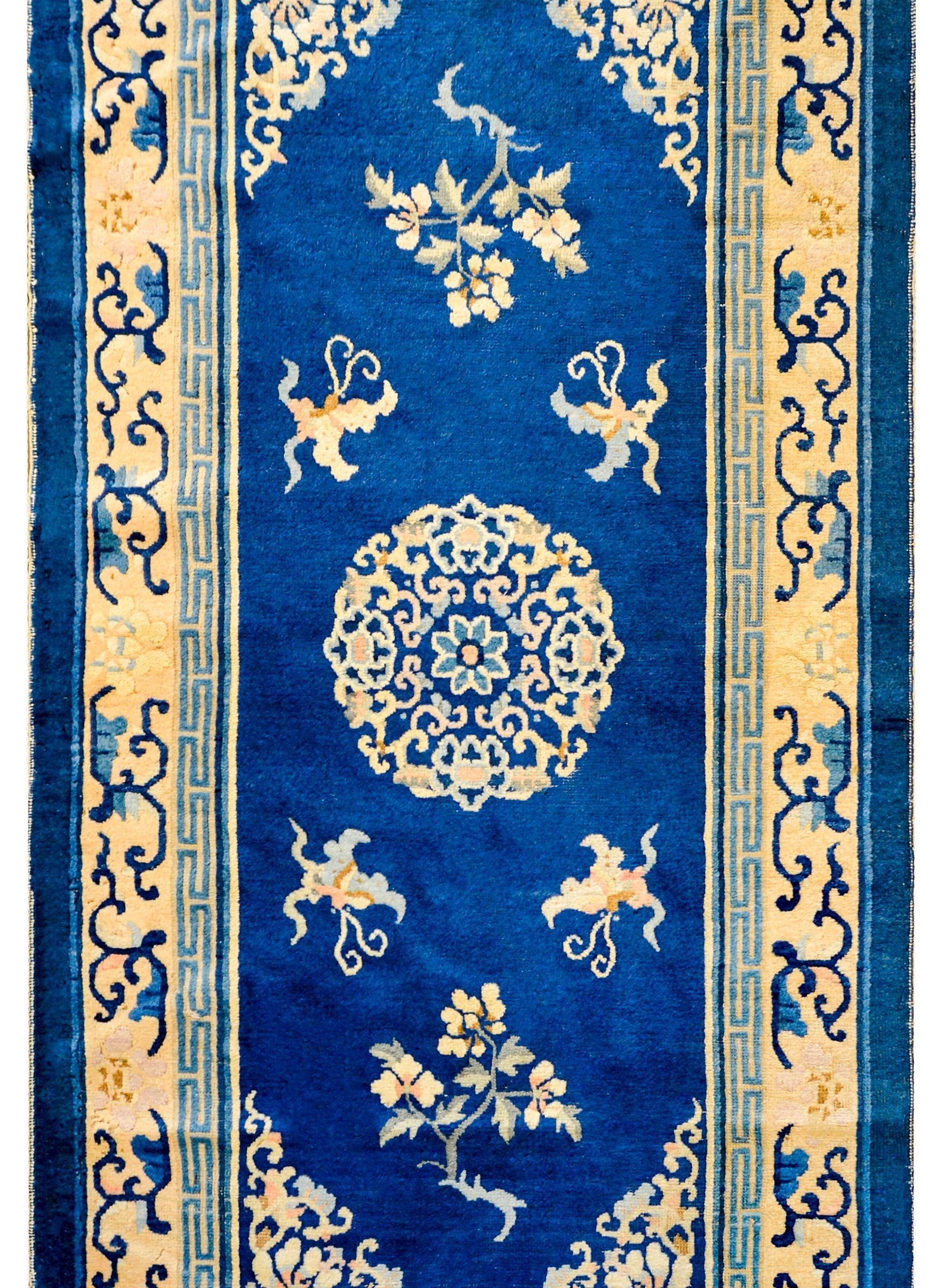 An early 20th century Chinese Peking rug woven in a fantastic indigo and cream color-way, with a large central peony and butterfly medallion amidst a field of chrysanthemums. The border is complex with two distinct peony and leafy vine patterned