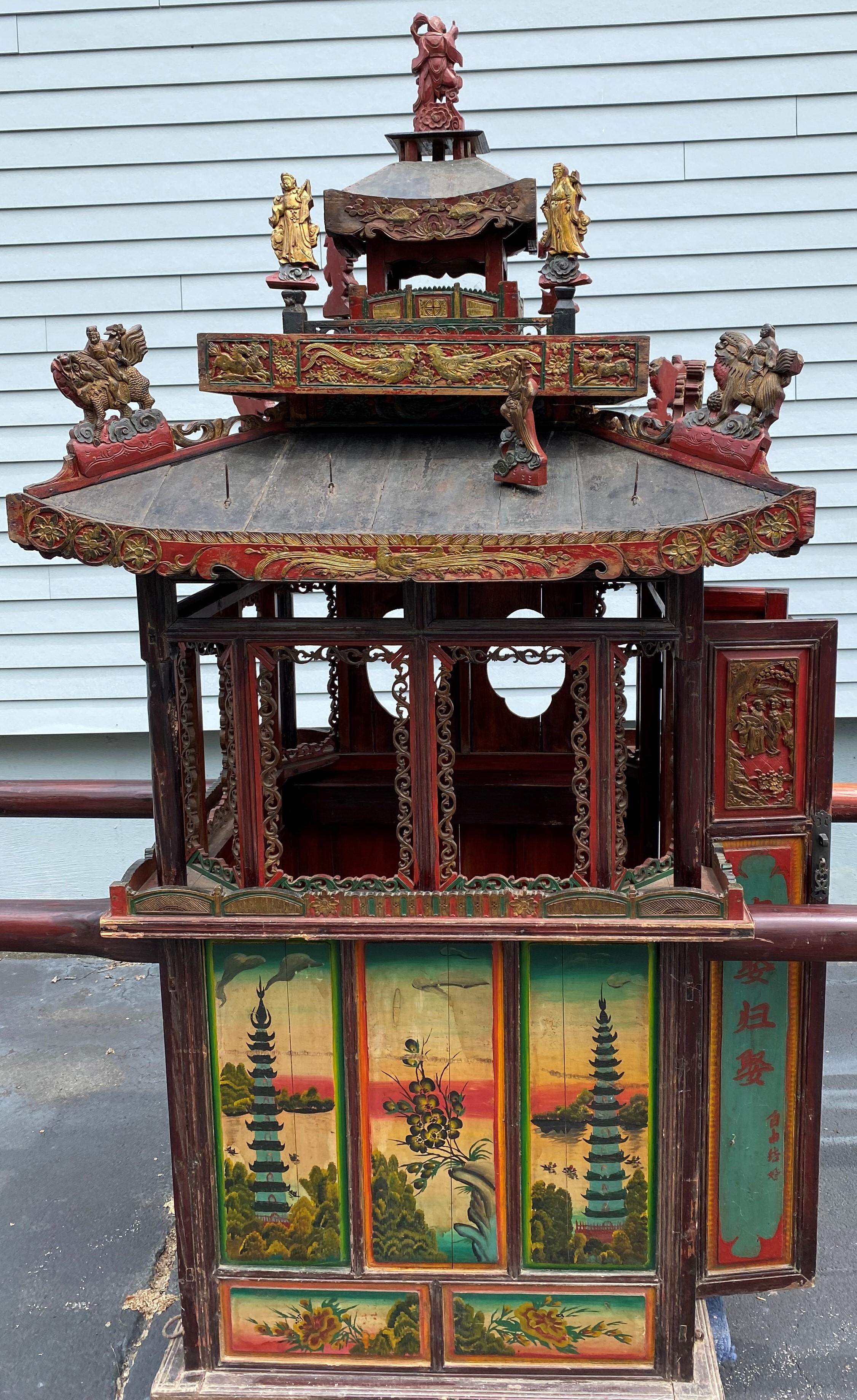 A fine example of an antique Chinese wedding sedan chair with lift poles, with removable pagoda style roof decorated with gilt carved figures and floral borders, surmounting a single seat red painted cabin with two decorated doors for the bride to
