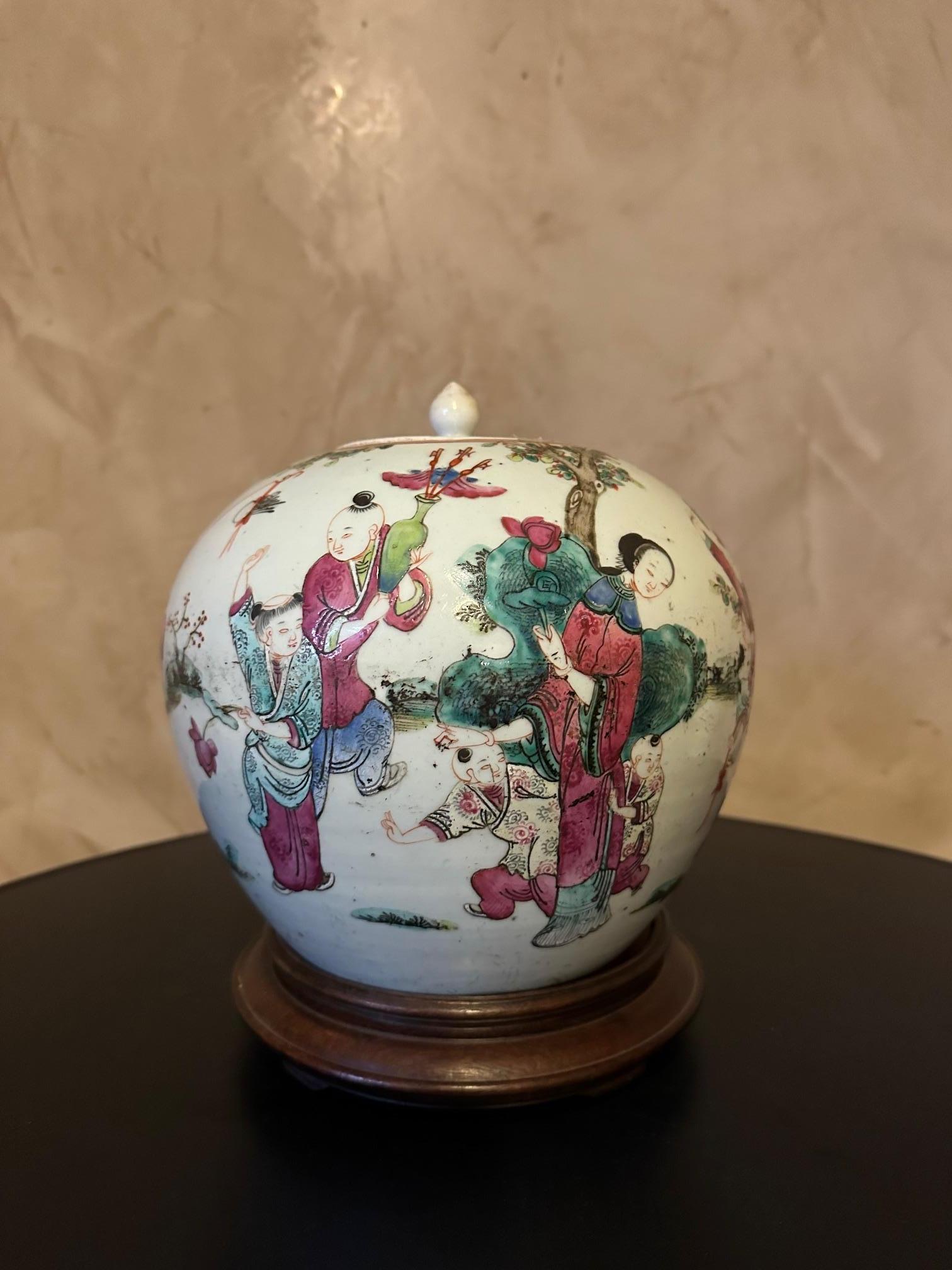Chinese Famille Rose enameled porcelain ginger pot dating from the beginning of the 20th century decorated with a woman surrounded by children playing in a garden. Paint slightly discolored over time.
Wooden base. Beautiful piece.