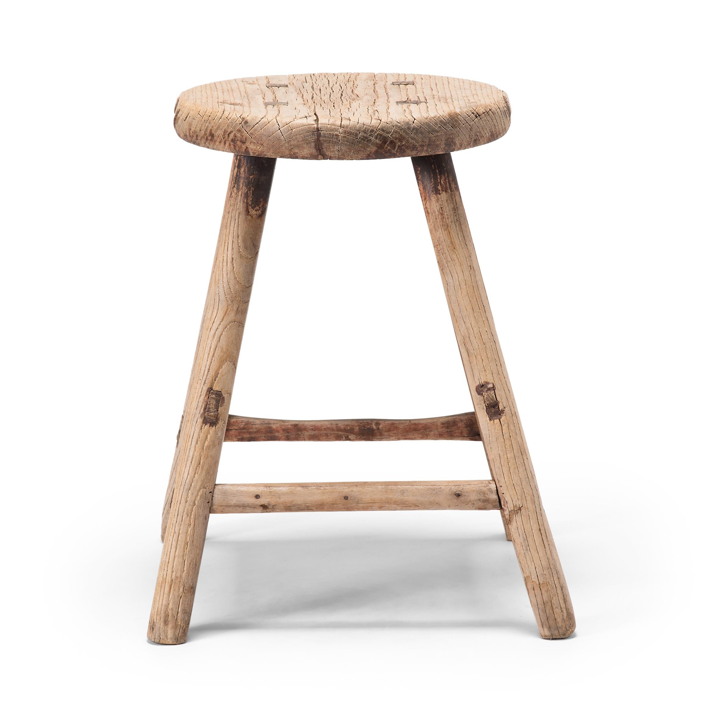 This early 20th century round-top stool from China's Shanxi province is beautiful in its simplicity. The stool's elmwood seat was flat-sawn to reveal grain patterns running parallel to the surface, the deep grooves accentuated by a century of use.