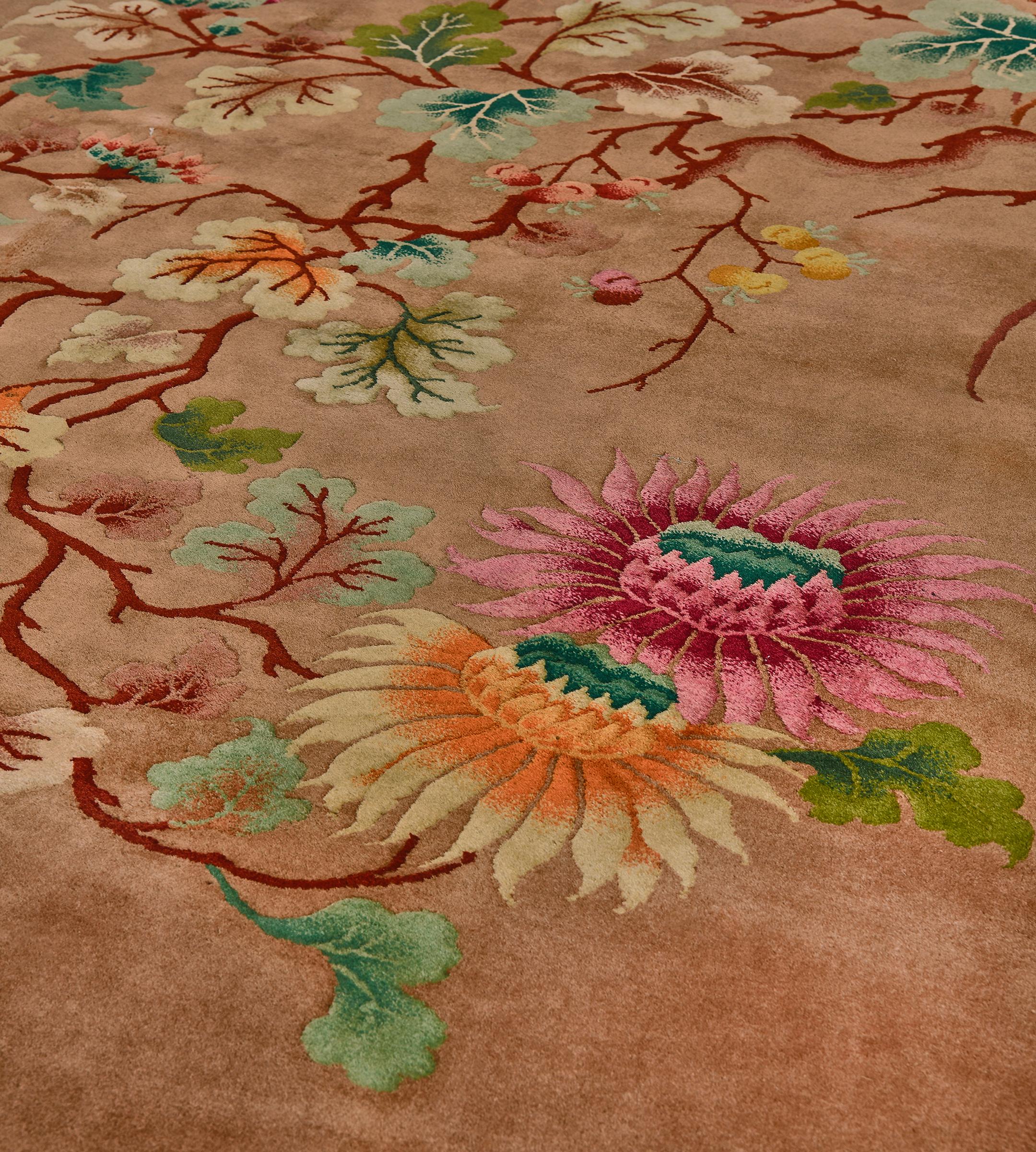 Ce tapis chinois traditionnel tissé à la main présente un champ café-au-lait avec des vignes rouille sinueuses émettant des tournesols polychromes et de délicates feuilles stylisées, dans une bordure unie rouge rouille.