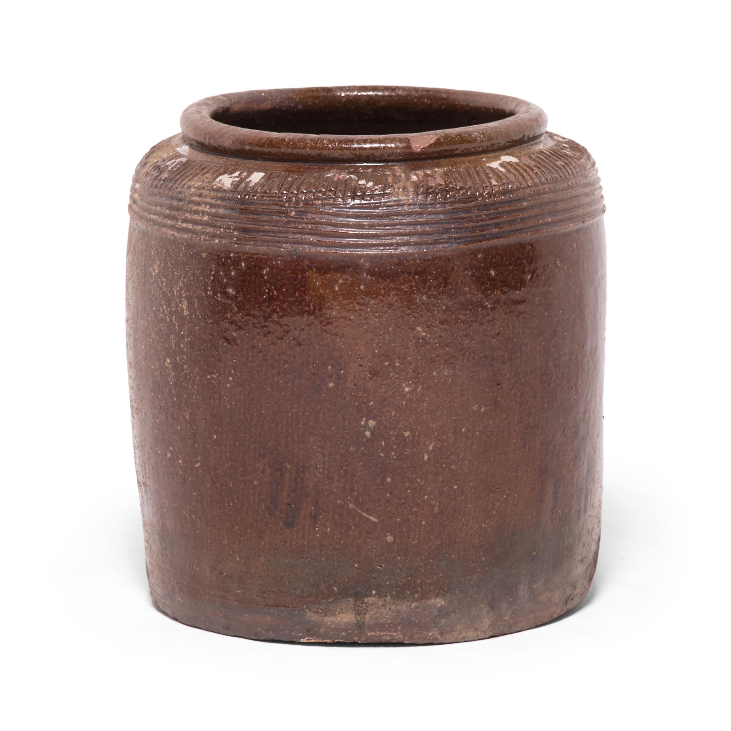 Originally used for salt pickling eggs and other foods, this early 20th century ceramic jar from China's Shanxi province is coated inside and out with a warm brown glaze. Decorative ridges pattern the jar's high shoulders and accentuate the rounded