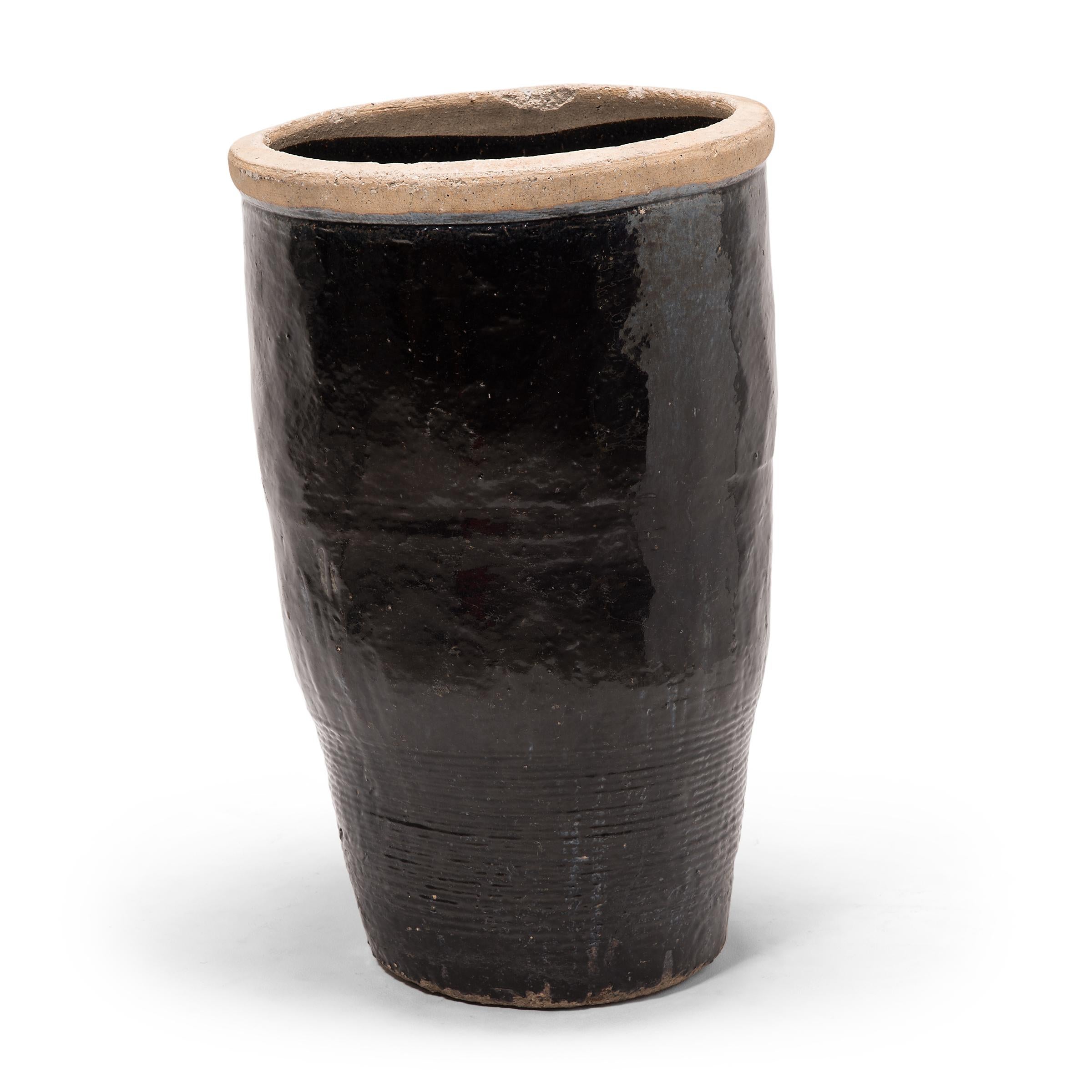 Originally used for pickling foods, this monumental early 20th century vessel is coated inside and out with a dark glaze. Subtle ridges at the base suggest that the jar was fashioned by coiling flattened ropes of clay into the desired shape.