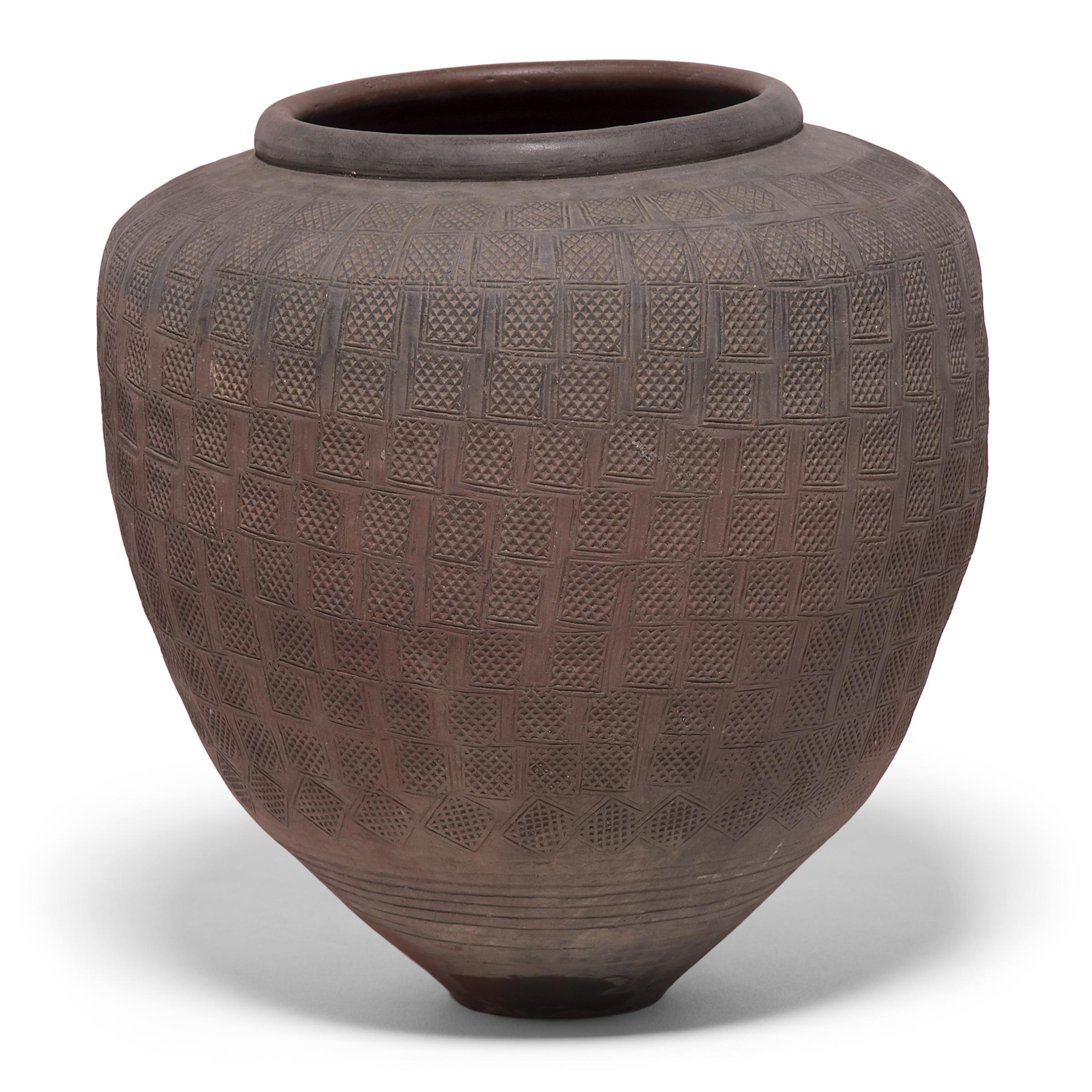 Charged with the humble task of pickling vegetables, this capacious earthenware jar is distinguished by its remarkable stamp pattern. Pressing a square stamp incised with a geometric pattern, the potter layered and staggered impressions to enliven