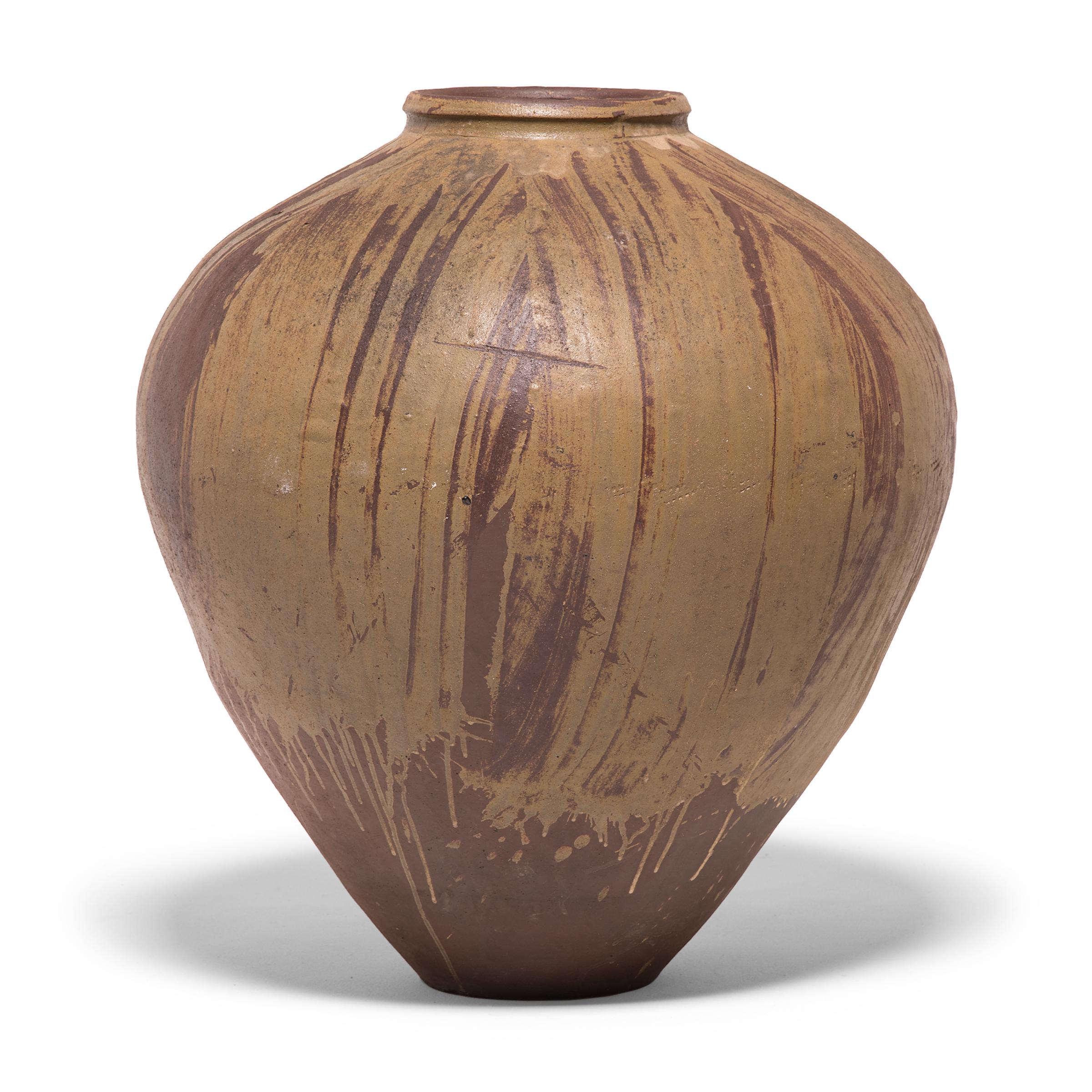 This early 20th century ceramic jar from China's Sichuan province is formed in a traditional shape meant for storing wine and spirits made from rice and grains. Applied with a loose hand, a light glaze sweeps across the jar's high shoulders, pooling