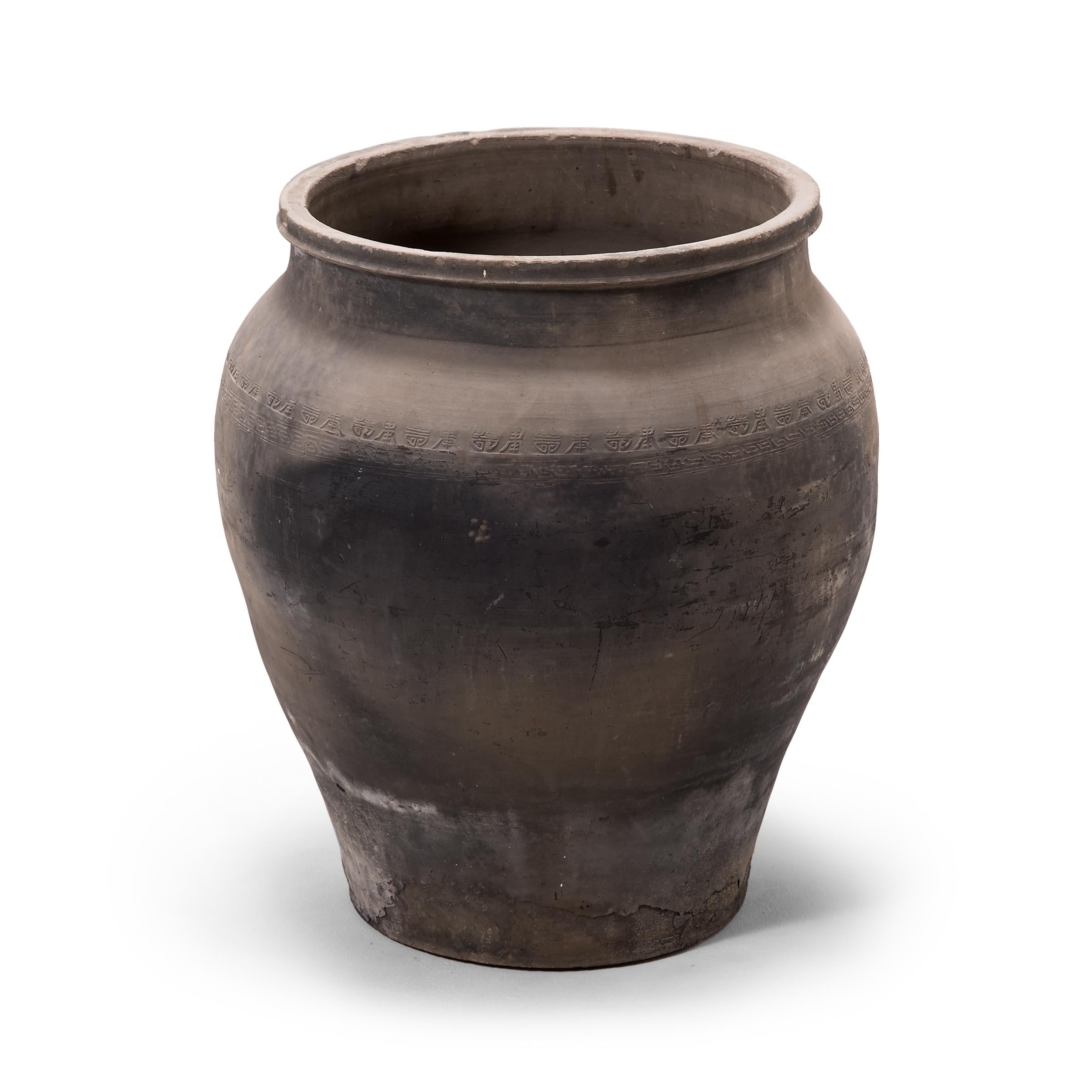 Charged with the humble task of storing dry goods, this capacious earthenware jar is distinguished by its tapered form and beautifully irregular unglazed surface. Smoke from the kiln gives the vessel its depth of color, transitioning gradually from