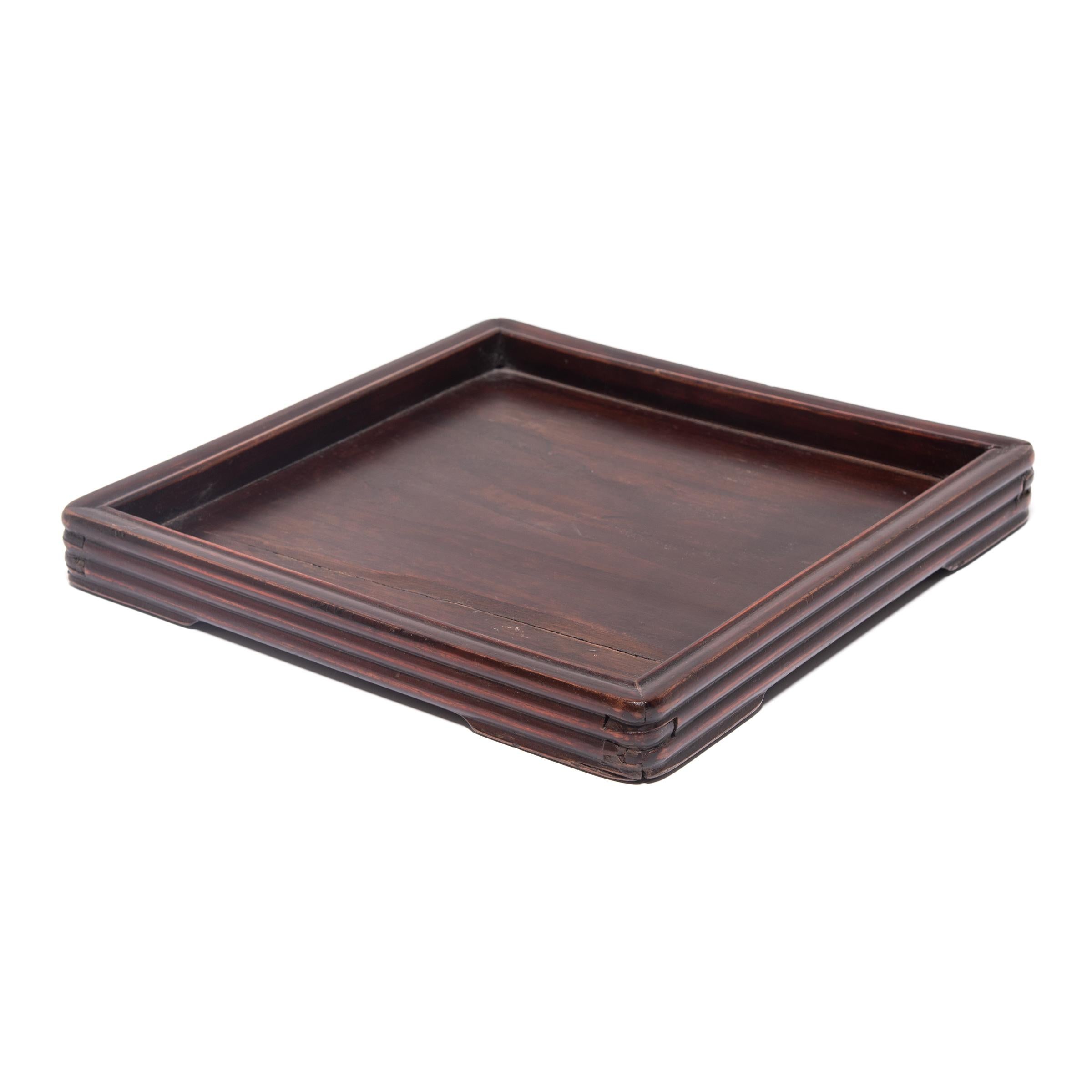 Simple lines, a modest form, and a layer of hand-brushed red lacquer give this Qing-dynasty footed tray a rustic charm that recalls the warmth of the home. The square tray is bordered by hand carved ridged edges, and iron fittings adorn the tray's