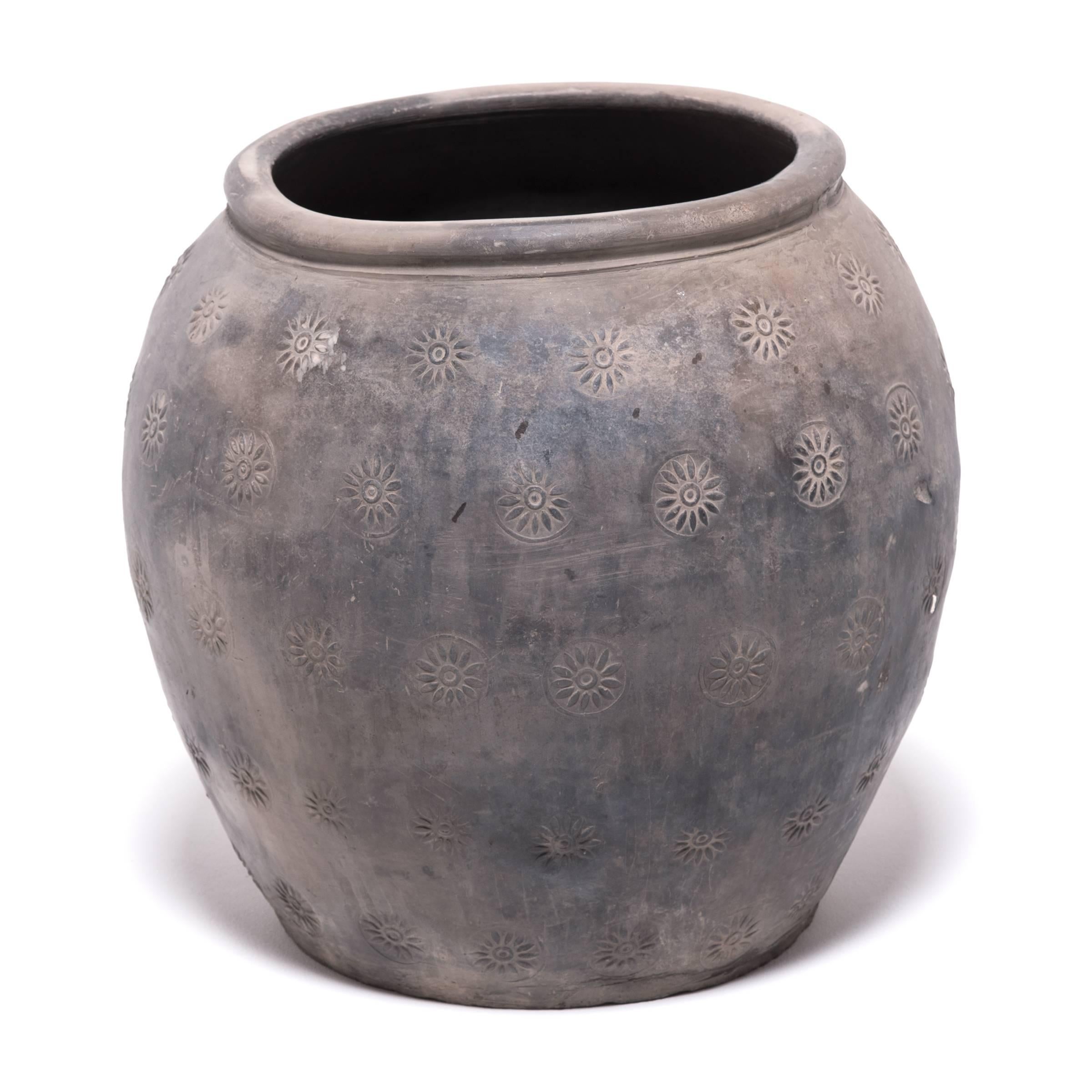 Over a century ago, a gifted potter from northern China crafted this organic clay jar out of rich dark river clay mined from the river basins of Asia. The surface is stamped with a series of simple floral patterns. The remaining clay is left