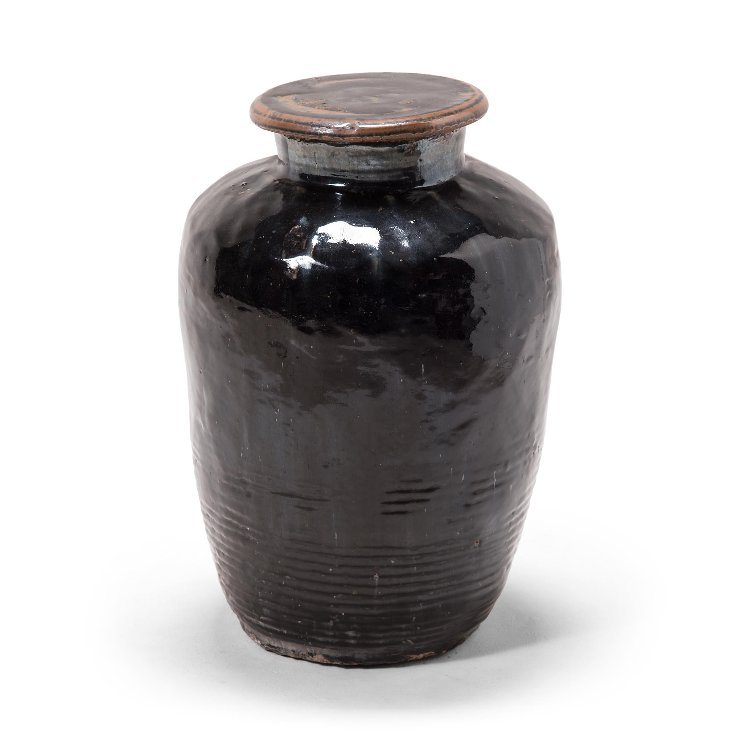 Originally used for fermenting rice or sorghum into vinegar, this monumental early 20th century vessel is coated inside and out with a dark glaze. The inky glaze sheets and pools over the jar's textured sides, lingering beautifully on every