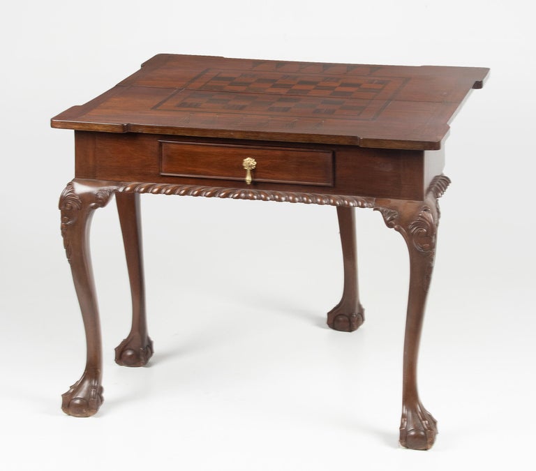 An English Chippendale style game/chess table with a flip-top. It can be used as a chess table and as a side table. The fold reveals a wood v enter inlay board. The table is supported by cabriole legs with claw legs. With a storage drawer for the