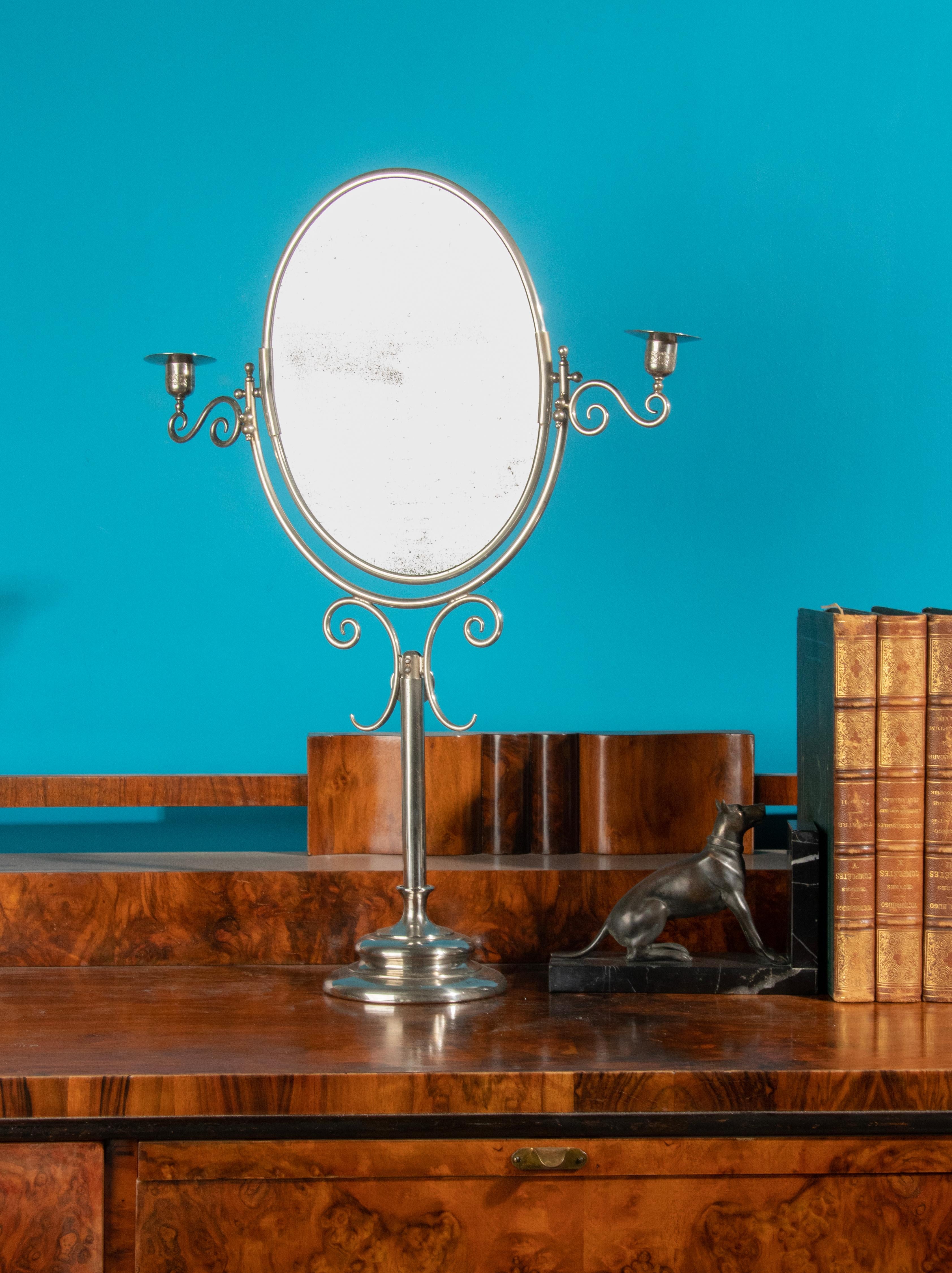 An elegant table vanity mirror. Made of chrome plated metal. The mirror are flanked with two candlesticks. The mirror is adjustable in height and the mirror can tilt. The mirror glass have some wear behind the glass, visibility is good. See