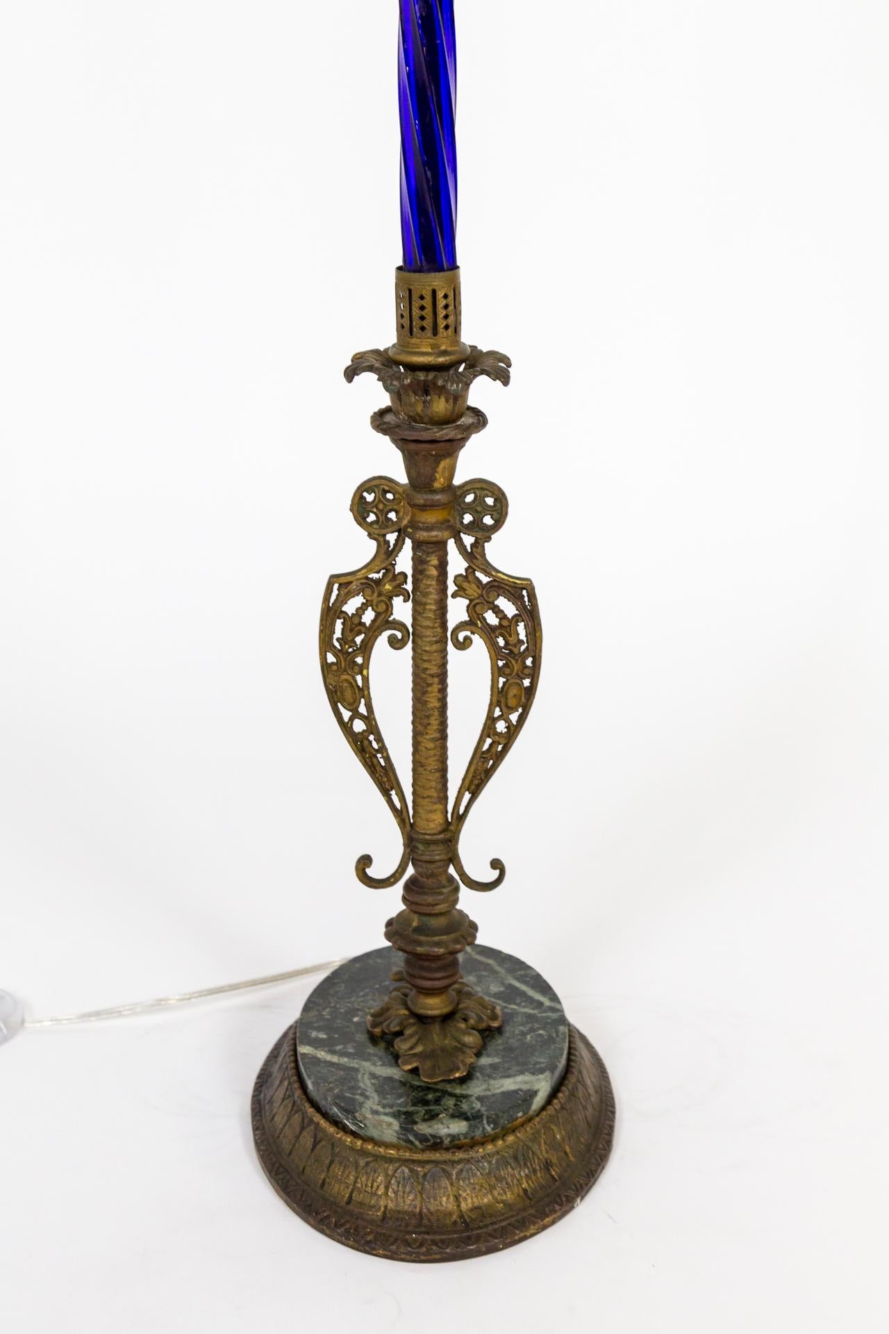Stehlampe im viktorianischen Stil, anglo-indisch inspiriert, auf einem ovalen Sockel aus Messing- und Marmorguss.
Der Hauptkörper ist aus auffälligem, 24 Zoll langem, gedrehtem, kobaltblauem Glas gefertigt, das in durchbrochene Messingkappen endet.